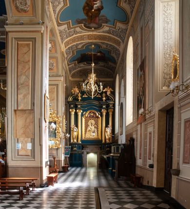 Zdjęcie nr 79: Kościół orientowany, murowany, trzynawowy. Typ halowy, z węższym, prostokątnym prezbiterium zamkniętym trójbocznie oraz z wieżą wbudowaną w zachodnią fasadę. Do prezbiterium od północy przylega zakrystia (do niej od zachodu klatka schodowa wiodąca do skarbca na piętrze), od południa natomiast kaplica Morsztynów z XVII wieku. Kaplica na planie prostokąta zamkniętego trójbocznie, z niszami w ściętych narożach, pod nią sklepiona krypta grobowa, opięta pilastrami wewnątrz i na zewnątrz. Od południa do korpusu przylega kruchta stanowiąca również kaplicę Matki Boskiej Pocieszenia. Korpus czteroprzęsłowy, nawy oddzielają arkady wsparte na filarach, pierwsze stanowią podparcie dla chóru. Nad nawami i prezbiterium strop imitujący sklepienie, na którym malowana dekoracja imitująca gurty, plafony oraz stiuki. Dekoracja ścian powtarza podziały wyznaczone przez arkady, namalowano na nich pilastry podtrzymujące belkowanie. W prezbiterium dwa okna usytuowane niedaleko ołtarza, w nawie osiem, wszystkie w kształcie stojącego prostokąta zamkniętego półkoliście, wypełnione witrażami z dekoracją geometryczną. Główne wejście od zachodu, drugie od północy, trzecie symetrycznie od południa przez kruchtę sklepioną kopułą, kolejne trzy do prezbiterium, od południa przez zakrystię i od północy przez kruchtę. 
Fasada zachodnia na cokole, podzielona gzymsami i lizenami, z wieżą zakończoną hełmem. Na osi drzwi w kształcie stojącego prostokąta flankowane prostokątnymi oknami, powyżej trzecie, większe okno zamknięte łukiem odcinkowym; kondygnację wieńczy gzyms. Druga kondygnacja powtarza podziały pierwszej. W środkowej osi okulus, powyżej dwudzielne okno zamknięte półkoliście. Nad nim tarcza zegara, kolejne dwie na ścianach bocznych. Kondygnacja ograniczona po bokach spływali wolutowymi i obeliskami zakończonymi kulami; przechodzi w wieżę. Powyżej gzyms podtrzymywany kroksztynami. Ostatnia kondygnacja o artykulacji ramowej z balkonami z każdej strony, powyżej wieńczącego gzymsu. Pozostałe elewacje na cokole, kontynuują podziały  lizenowo-ramowe, artykulacją podkreślają okna. Kaplica Morsztynów opięta pilastrami z głowicami, prezbiterium oszkarpowane. Dach nad nawą główną, kaplicą i prezbiterium dwuspadowy, na kruchtą południową kopuła, na wieży ozdobny hełm dołem wklęsły, dekorowany wolutami. Powyżej kopuła, na której latarnia przepruta arkadami i zwieńczona przewężoną w środku kopułą zakończoną ostrosłupem z kulą i krzyżem. 
Do najcenniejszych zabytków świątyni należą m.in. zaprojektowana przez Jana Delamarsa kaplica Morsztynów dekorowana stiukami z 1693 roku autorstwa Baltazara Fontany. Wewnątrz niej warto zwrócić uwagę na osiemnastowieczny ołtarz z przedstawieniem Oblicza Chrystusa i rzeźbionym antepedium. W ołtarz Ukrzyżowania znajdujący się w północnej nawie kościoła wkomponowano gotyckie rzeźby św. Jana i Marii. 