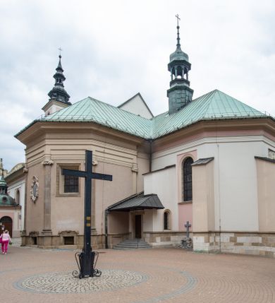 Zdjęcie nr 17: Kościół orientowany, murowany, trzynawowy. Typ halowy, z węższym, prostokątnym prezbiterium zamkniętym trójbocznie oraz z wieżą wbudowaną w zachodnią fasadę. Do prezbiterium od północy przylega zakrystia (do niej od zachodu klatka schodowa wiodąca do skarbca na piętrze), od południa natomiast kaplica Morsztynów z XVII wieku. Kaplica na planie prostokąta zamkniętego trójbocznie, z niszami w ściętych narożach, pod nią sklepiona krypta grobowa, opięta pilastrami wewnątrz i na zewnątrz. Od południa do korpusu przylega kruchta stanowiąca również kaplicę Matki Boskiej Pocieszenia. Korpus czteroprzęsłowy, nawy oddzielają arkady wsparte na filarach, pierwsze stanowią podparcie dla chóru. Nad nawami i prezbiterium strop imitujący sklepienie, na którym malowana dekoracja imitująca gurty, plafony oraz stiuki. Dekoracja ścian powtarza podziały wyznaczone przez arkady, namalowano na nich pilastry podtrzymujące belkowanie. W prezbiterium dwa okna usytuowane niedaleko ołtarza, w nawie osiem, wszystkie w kształcie stojącego prostokąta zamkniętego półkoliście, wypełnione witrażami z dekoracją geometryczną. Główne wejście od zachodu, drugie od północy, trzecie symetrycznie od południa przez kruchtę sklepioną kopułą, kolejne trzy do prezbiterium, od południa przez zakrystię i od północy przez kruchtę. 
Fasada zachodnia na cokole, podzielona gzymsami i lizenami, z wieżą zakończoną hełmem. Na osi drzwi w kształcie stojącego prostokąta flankowane prostokątnymi oknami, powyżej trzecie, większe okno zamknięte łukiem odcinkowym; kondygnację wieńczy gzyms. Druga kondygnacja powtarza podziały pierwszej. W środkowej osi okulus, powyżej dwudzielne okno zamknięte półkoliście. Nad nim tarcza zegara, kolejne dwie na ścianach bocznych. Kondygnacja ograniczona po bokach spływali wolutowymi i obeliskami zakończonymi kulami; przechodzi w wieżę. Powyżej gzyms podtrzymywany kroksztynami. Ostatnia kondygnacja o artykulacji ramowej z balkonami z każdej strony, powyżej wieńczącego gzymsu. Pozostałe elewacje na cokole, kontynuują podziały  lizenowo-ramowe, artykulacją podkreślają okna. Kaplica Morsztynów opięta pilastrami z głowicami, prezbiterium oszkarpowane. Dach nad nawą główną, kaplicą i prezbiterium dwuspadowy, na kruchtą południową kopuła, na wieży ozdobny hełm dołem wklęsły, dekorowany wolutami. Powyżej kopuła, na której latarnia przepruta arkadami i zwieńczona przewężoną w środku kopułą zakończoną ostrosłupem z kulą i krzyżem. 
Do najcenniejszych zabytków świątyni należą m.in. zaprojektowana przez Jana Delamarsa kaplica Morsztynów dekorowana stiukami z 1693 roku autorstwa Baltazara Fontany. Wewnątrz niej warto zwrócić uwagę na osiemnastowieczny ołtarz z przedstawieniem Oblicza Chrystusa i rzeźbionym antepedium. W ołtarz Ukrzyżowania znajdujący się w północnej nawie kościoła wkomponowano gotyckie rzeźby św. Jana i Marii. 