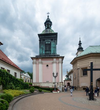 Zdjęcie nr 34: Kościół orientowany, murowany, trzynawowy. Typ halowy, z węższym, prostokątnym prezbiterium zamkniętym trójbocznie oraz z wieżą wbudowaną w zachodnią fasadę. Do prezbiterium od północy przylega zakrystia (do niej od zachodu klatka schodowa wiodąca do skarbca na piętrze), od południa natomiast kaplica Morsztynów z XVII wieku. Kaplica na planie prostokąta zamkniętego trójbocznie, z niszami w ściętych narożach, pod nią sklepiona krypta grobowa, opięta pilastrami wewnątrz i na zewnątrz. Od południa do korpusu przylega kruchta stanowiąca również kaplicę Matki Boskiej Pocieszenia. Korpus czteroprzęsłowy, nawy oddzielają arkady wsparte na filarach, pierwsze stanowią podparcie dla chóru. Nad nawami i prezbiterium strop imitujący sklepienie, na którym malowana dekoracja imitująca gurty, plafony oraz stiuki. Dekoracja ścian powtarza podziały wyznaczone przez arkady, namalowano na nich pilastry podtrzymujące belkowanie. W prezbiterium dwa okna usytuowane niedaleko ołtarza, w nawie osiem, wszystkie w kształcie stojącego prostokąta zamkniętego półkoliście, wypełnione witrażami z dekoracją geometryczną. Główne wejście od zachodu, drugie od północy, trzecie symetrycznie od południa przez kruchtę sklepioną kopułą, kolejne trzy do prezbiterium, od południa przez zakrystię i od północy przez kruchtę. 
Fasada zachodnia na cokole, podzielona gzymsami i lizenami, z wieżą zakończoną hełmem. Na osi drzwi w kształcie stojącego prostokąta flankowane prostokątnymi oknami, powyżej trzecie, większe okno zamknięte łukiem odcinkowym; kondygnację wieńczy gzyms. Druga kondygnacja powtarza podziały pierwszej. W środkowej osi okulus, powyżej dwudzielne okno zamknięte półkoliście. Nad nim tarcza zegara, kolejne dwie na ścianach bocznych. Kondygnacja ograniczona po bokach spływali wolutowymi i obeliskami zakończonymi kulami; przechodzi w wieżę. Powyżej gzyms podtrzymywany kroksztynami. Ostatnia kondygnacja o artykulacji ramowej z balkonami z każdej strony, powyżej wieńczącego gzymsu. Pozostałe elewacje na cokole, kontynuują podziały  lizenowo-ramowe, artykulacją podkreślają okna. Kaplica Morsztynów opięta pilastrami z głowicami, prezbiterium oszkarpowane. Dach nad nawą główną, kaplicą i prezbiterium dwuspadowy, na kruchtą południową kopuła, na wieży ozdobny hełm dołem wklęsły, dekorowany wolutami. Powyżej kopuła, na której latarnia przepruta arkadami i zwieńczona przewężoną w środku kopułą zakończoną ostrosłupem z kulą i krzyżem. 
Do najcenniejszych zabytków świątyni należą m.in. zaprojektowana przez Jana Delamarsa kaplica Morsztynów dekorowana stiukami z 1693 roku autorstwa Baltazara Fontany. Wewnątrz niej warto zwrócić uwagę na osiemnastowieczny ołtarz z przedstawieniem Oblicza Chrystusa i rzeźbionym antepedium. W ołtarz Ukrzyżowania znajdujący się w północnej nawie kościoła wkomponowano gotyckie rzeźby św. Jana i Marii. 