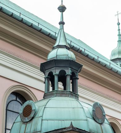 Zdjęcie nr 42: Kościół orientowany, murowany, trzynawowy. Typ halowy, z węższym, prostokątnym prezbiterium zamkniętym trójbocznie oraz z wieżą wbudowaną w zachodnią fasadę. Do prezbiterium od północy przylega zakrystia (do niej od zachodu klatka schodowa wiodąca do skarbca na piętrze), od południa natomiast kaplica Morsztynów z XVII wieku. Kaplica na planie prostokąta zamkniętego trójbocznie, z niszami w ściętych narożach, pod nią sklepiona krypta grobowa, opięta pilastrami wewnątrz i na zewnątrz. Od południa do korpusu przylega kruchta stanowiąca również kaplicę Matki Boskiej Pocieszenia. Korpus czteroprzęsłowy, nawy oddzielają arkady wsparte na filarach, pierwsze stanowią podparcie dla chóru. Nad nawami i prezbiterium strop imitujący sklepienie, na którym malowana dekoracja imitująca gurty, plafony oraz stiuki. Dekoracja ścian powtarza podziały wyznaczone przez arkady, namalowano na nich pilastry podtrzymujące belkowanie. W prezbiterium dwa okna usytuowane niedaleko ołtarza, w nawie osiem, wszystkie w kształcie stojącego prostokąta zamkniętego półkoliście, wypełnione witrażami z dekoracją geometryczną. Główne wejście od zachodu, drugie od północy, trzecie symetrycznie od południa przez kruchtę sklepioną kopułą, kolejne trzy do prezbiterium, od południa przez zakrystię i od północy przez kruchtę. 
Fasada zachodnia na cokole, podzielona gzymsami i lizenami, z wieżą zakończoną hełmem. Na osi drzwi w kształcie stojącego prostokąta flankowane prostokątnymi oknami, powyżej trzecie, większe okno zamknięte łukiem odcinkowym; kondygnację wieńczy gzyms. Druga kondygnacja powtarza podziały pierwszej. W środkowej osi okulus, powyżej dwudzielne okno zamknięte półkoliście. Nad nim tarcza zegara, kolejne dwie na ścianach bocznych. Kondygnacja ograniczona po bokach spływali wolutowymi i obeliskami zakończonymi kulami; przechodzi w wieżę. Powyżej gzyms podtrzymywany kroksztynami. Ostatnia kondygnacja o artykulacji ramowej z balkonami z każdej strony, powyżej wieńczącego gzymsu. Pozostałe elewacje na cokole, kontynuują podziały  lizenowo-ramowe, artykulacją podkreślają okna. Kaplica Morsztynów opięta pilastrami z głowicami, prezbiterium oszkarpowane. Dach nad nawą główną, kaplicą i prezbiterium dwuspadowy, na kruchtą południową kopuła, na wieży ozdobny hełm dołem wklęsły, dekorowany wolutami. Powyżej kopuła, na której latarnia przepruta arkadami i zwieńczona przewężoną w środku kopułą zakończoną ostrosłupem z kulą i krzyżem. 
Do najcenniejszych zabytków świątyni należą m.in. zaprojektowana przez Jana Delamarsa kaplica Morsztynów dekorowana stiukami z 1693 roku autorstwa Baltazara Fontany. Wewnątrz niej warto zwrócić uwagę na osiemnastowieczny ołtarz z przedstawieniem Oblicza Chrystusa i rzeźbionym antepedium. W ołtarz Ukrzyżowania znajdujący się w północnej nawie kościoła wkomponowano gotyckie rzeźby św. Jana i Marii. 