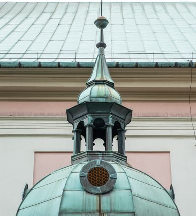 Zdjęcie nr 33: Kościół orientowany, murowany, trzynawowy. Typ halowy, z węższym, prostokątnym prezbiterium zamkniętym trójbocznie oraz z wieżą wbudowaną w zachodnią fasadę. Do prezbiterium od północy przylega zakrystia (do niej od zachodu klatka schodowa wiodąca do skarbca na piętrze), od południa natomiast kaplica Morsztynów z XVII wieku. Kaplica na planie prostokąta zamkniętego trójbocznie, z niszami w ściętych narożach, pod nią sklepiona krypta grobowa, opięta pilastrami wewnątrz i na zewnątrz. Od południa do korpusu przylega kruchta stanowiąca również kaplicę Matki Boskiej Pocieszenia. Korpus czteroprzęsłowy, nawy oddzielają arkady wsparte na filarach, pierwsze stanowią podparcie dla chóru. Nad nawami i prezbiterium strop imitujący sklepienie, na którym malowana dekoracja imitująca gurty, plafony oraz stiuki. Dekoracja ścian powtarza podziały wyznaczone przez arkady, namalowano na nich pilastry podtrzymujące belkowanie. W prezbiterium dwa okna usytuowane niedaleko ołtarza, w nawie osiem, wszystkie w kształcie stojącego prostokąta zamkniętego półkoliście, wypełnione witrażami z dekoracją geometryczną. Główne wejście od zachodu, drugie od północy, trzecie symetrycznie od południa przez kruchtę sklepioną kopułą, kolejne trzy do prezbiterium, od południa przez zakrystię i od północy przez kruchtę. 
Fasada zachodnia na cokole, podzielona gzymsami i lizenami, z wieżą zakończoną hełmem. Na osi drzwi w kształcie stojącego prostokąta flankowane prostokątnymi oknami, powyżej trzecie, większe okno zamknięte łukiem odcinkowym; kondygnację wieńczy gzyms. Druga kondygnacja powtarza podziały pierwszej. W środkowej osi okulus, powyżej dwudzielne okno zamknięte półkoliście. Nad nim tarcza zegara, kolejne dwie na ścianach bocznych. Kondygnacja ograniczona po bokach spływali wolutowymi i obeliskami zakończonymi kulami; przechodzi w wieżę. Powyżej gzyms podtrzymywany kroksztynami. Ostatnia kondygnacja o artykulacji ramowej z balkonami z każdej strony, powyżej wieńczącego gzymsu. Pozostałe elewacje na cokole, kontynuują podziały  lizenowo-ramowe, artykulacją podkreślają okna. Kaplica Morsztynów opięta pilastrami z głowicami, prezbiterium oszkarpowane. Dach nad nawą główną, kaplicą i prezbiterium dwuspadowy, na kruchtą południową kopuła, na wieży ozdobny hełm dołem wklęsły, dekorowany wolutami. Powyżej kopuła, na której latarnia przepruta arkadami i zwieńczona przewężoną w środku kopułą zakończoną ostrosłupem z kulą i krzyżem. 
Do najcenniejszych zabytków świątyni należą m.in. zaprojektowana przez Jana Delamarsa kaplica Morsztynów dekorowana stiukami z 1693 roku autorstwa Baltazara Fontany. Wewnątrz niej warto zwrócić uwagę na osiemnastowieczny ołtarz z przedstawieniem Oblicza Chrystusa i rzeźbionym antepedium. W ołtarz Ukrzyżowania znajdujący się w północnej nawie kościoła wkomponowano gotyckie rzeźby św. Jana i Marii. 