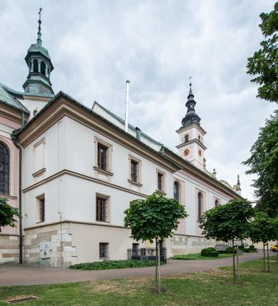 Zdjęcie nr 47: Kościół orientowany, murowany, trzynawowy. Typ halowy, z węższym, prostokątnym prezbiterium zamkniętym trójbocznie oraz z wieżą wbudowaną w zachodnią fasadę. Do prezbiterium od północy przylega zakrystia (do niej od zachodu klatka schodowa wiodąca do skarbca na piętrze), od południa natomiast kaplica Morsztynów z XVII wieku. Kaplica na planie prostokąta zamkniętego trójbocznie, z niszami w ściętych narożach, pod nią sklepiona krypta grobowa, opięta pilastrami wewnątrz i na zewnątrz. Od południa do korpusu przylega kruchta stanowiąca również kaplicę Matki Boskiej Pocieszenia. Korpus czteroprzęsłowy, nawy oddzielają arkady wsparte na filarach, pierwsze stanowią podparcie dla chóru. Nad nawami i prezbiterium strop imitujący sklepienie, na którym malowana dekoracja imitująca gurty, plafony oraz stiuki. Dekoracja ścian powtarza podziały wyznaczone przez arkady, namalowano na nich pilastry podtrzymujące belkowanie. W prezbiterium dwa okna usytuowane niedaleko ołtarza, w nawie osiem, wszystkie w kształcie stojącego prostokąta zamkniętego półkoliście, wypełnione witrażami z dekoracją geometryczną. Główne wejście od zachodu, drugie od północy, trzecie symetrycznie od południa przez kruchtę sklepioną kopułą, kolejne trzy do prezbiterium, od południa przez zakrystię i od północy przez kruchtę. 
Fasada zachodnia na cokole, podzielona gzymsami i lizenami, z wieżą zakończoną hełmem. Na osi drzwi w kształcie stojącego prostokąta flankowane prostokątnymi oknami, powyżej trzecie, większe okno zamknięte łukiem odcinkowym; kondygnację wieńczy gzyms. Druga kondygnacja powtarza podziały pierwszej. W środkowej osi okulus, powyżej dwudzielne okno zamknięte półkoliście. Nad nim tarcza zegara, kolejne dwie na ścianach bocznych. Kondygnacja ograniczona po bokach spływali wolutowymi i obeliskami zakończonymi kulami; przechodzi w wieżę. Powyżej gzyms podtrzymywany kroksztynami. Ostatnia kondygnacja o artykulacji ramowej z balkonami z każdej strony, powyżej wieńczącego gzymsu. Pozostałe elewacje na cokole, kontynuują podziały  lizenowo-ramowe, artykulacją podkreślają okna. Kaplica Morsztynów opięta pilastrami z głowicami, prezbiterium oszkarpowane. Dach nad nawą główną, kaplicą i prezbiterium dwuspadowy, na kruchtą południową kopuła, na wieży ozdobny hełm dołem wklęsły, dekorowany wolutami. Powyżej kopuła, na której latarnia przepruta arkadami i zwieńczona przewężoną w środku kopułą zakończoną ostrosłupem z kulą i krzyżem. 
Do najcenniejszych zabytków świątyni należą m.in. zaprojektowana przez Jana Delamarsa kaplica Morsztynów dekorowana stiukami z 1693 roku autorstwa Baltazara Fontany. Wewnątrz niej warto zwrócić uwagę na osiemnastowieczny ołtarz z przedstawieniem Oblicza Chrystusa i rzeźbionym antepedium. W ołtarz Ukrzyżowania znajdujący się w północnej nawie kościoła wkomponowano gotyckie rzeźby św. Jana i Marii. 