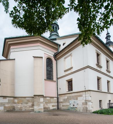 Zdjęcie nr 15: Kościół orientowany, murowany, trzynawowy. Typ halowy, z węższym, prostokątnym prezbiterium zamkniętym trójbocznie oraz z wieżą wbudowaną w zachodnią fasadę. Do prezbiterium od północy przylega zakrystia (do niej od zachodu klatka schodowa wiodąca do skarbca na piętrze), od południa natomiast kaplica Morsztynów z XVII wieku. Kaplica na planie prostokąta zamkniętego trójbocznie, z niszami w ściętych narożach, pod nią sklepiona krypta grobowa, opięta pilastrami wewnątrz i na zewnątrz. Od południa do korpusu przylega kruchta stanowiąca również kaplicę Matki Boskiej Pocieszenia. Korpus czteroprzęsłowy, nawy oddzielają arkady wsparte na filarach, pierwsze stanowią podparcie dla chóru. Nad nawami i prezbiterium strop imitujący sklepienie, na którym malowana dekoracja imitująca gurty, plafony oraz stiuki. Dekoracja ścian powtarza podziały wyznaczone przez arkady, namalowano na nich pilastry podtrzymujące belkowanie. W prezbiterium dwa okna usytuowane niedaleko ołtarza, w nawie osiem, wszystkie w kształcie stojącego prostokąta zamkniętego półkoliście, wypełnione witrażami z dekoracją geometryczną. Główne wejście od zachodu, drugie od północy, trzecie symetrycznie od południa przez kruchtę sklepioną kopułą, kolejne trzy do prezbiterium, od południa przez zakrystię i od północy przez kruchtę. 
Fasada zachodnia na cokole, podzielona gzymsami i lizenami, z wieżą zakończoną hełmem. Na osi drzwi w kształcie stojącego prostokąta flankowane prostokątnymi oknami, powyżej trzecie, większe okno zamknięte łukiem odcinkowym; kondygnację wieńczy gzyms. Druga kondygnacja powtarza podziały pierwszej. W środkowej osi okulus, powyżej dwudzielne okno zamknięte półkoliście. Nad nim tarcza zegara, kolejne dwie na ścianach bocznych. Kondygnacja ograniczona po bokach spływali wolutowymi i obeliskami zakończonymi kulami; przechodzi w wieżę. Powyżej gzyms podtrzymywany kroksztynami. Ostatnia kondygnacja o artykulacji ramowej z balkonami z każdej strony, powyżej wieńczącego gzymsu. Pozostałe elewacje na cokole, kontynuują podziały  lizenowo-ramowe, artykulacją podkreślają okna. Kaplica Morsztynów opięta pilastrami z głowicami, prezbiterium oszkarpowane. Dach nad nawą główną, kaplicą i prezbiterium dwuspadowy, na kruchtą południową kopuła, na wieży ozdobny hełm dołem wklęsły, dekorowany wolutami. Powyżej kopuła, na której latarnia przepruta arkadami i zwieńczona przewężoną w środku kopułą zakończoną ostrosłupem z kulą i krzyżem. 
Do najcenniejszych zabytków świątyni należą m.in. zaprojektowana przez Jana Delamarsa kaplica Morsztynów dekorowana stiukami z 1693 roku autorstwa Baltazara Fontany. Wewnątrz niej warto zwrócić uwagę na osiemnastowieczny ołtarz z przedstawieniem Oblicza Chrystusa i rzeźbionym antepedium. W ołtarz Ukrzyżowania znajdujący się w północnej nawie kościoła wkomponowano gotyckie rzeźby św. Jana i Marii. 