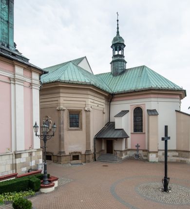 Zdjęcie nr 19: Kościół orientowany, murowany, trzynawowy. Typ halowy, z węższym, prostokątnym prezbiterium zamkniętym trójbocznie oraz z wieżą wbudowaną w zachodnią fasadę. Do prezbiterium od północy przylega zakrystia (do niej od zachodu klatka schodowa wiodąca do skarbca na piętrze), od południa natomiast kaplica Morsztynów z XVII wieku. Kaplica na planie prostokąta zamkniętego trójbocznie, z niszami w ściętych narożach, pod nią sklepiona krypta grobowa, opięta pilastrami wewnątrz i na zewnątrz. Od południa do korpusu przylega kruchta stanowiąca również kaplicę Matki Boskiej Pocieszenia. Korpus czteroprzęsłowy, nawy oddzielają arkady wsparte na filarach, pierwsze stanowią podparcie dla chóru. Nad nawami i prezbiterium strop imitujący sklepienie, na którym malowana dekoracja imitująca gurty, plafony oraz stiuki. Dekoracja ścian powtarza podziały wyznaczone przez arkady, namalowano na nich pilastry podtrzymujące belkowanie. W prezbiterium dwa okna usytuowane niedaleko ołtarza, w nawie osiem, wszystkie w kształcie stojącego prostokąta zamkniętego półkoliście, wypełnione witrażami z dekoracją geometryczną. Główne wejście od zachodu, drugie od północy, trzecie symetrycznie od południa przez kruchtę sklepioną kopułą, kolejne trzy do prezbiterium, od południa przez zakrystię i od północy przez kruchtę. 
Fasada zachodnia na cokole, podzielona gzymsami i lizenami, z wieżą zakończoną hełmem. Na osi drzwi w kształcie stojącego prostokąta flankowane prostokątnymi oknami, powyżej trzecie, większe okno zamknięte łukiem odcinkowym; kondygnację wieńczy gzyms. Druga kondygnacja powtarza podziały pierwszej. W środkowej osi okulus, powyżej dwudzielne okno zamknięte półkoliście. Nad nim tarcza zegara, kolejne dwie na ścianach bocznych. Kondygnacja ograniczona po bokach spływali wolutowymi i obeliskami zakończonymi kulami; przechodzi w wieżę. Powyżej gzyms podtrzymywany kroksztynami. Ostatnia kondygnacja o artykulacji ramowej z balkonami z każdej strony, powyżej wieńczącego gzymsu. Pozostałe elewacje na cokole, kontynuują podziały  lizenowo-ramowe, artykulacją podkreślają okna. Kaplica Morsztynów opięta pilastrami z głowicami, prezbiterium oszkarpowane. Dach nad nawą główną, kaplicą i prezbiterium dwuspadowy, na kruchtą południową kopuła, na wieży ozdobny hełm dołem wklęsły, dekorowany wolutami. Powyżej kopuła, na której latarnia przepruta arkadami i zwieńczona przewężoną w środku kopułą zakończoną ostrosłupem z kulą i krzyżem. 
Do najcenniejszych zabytków świątyni należą m.in. zaprojektowana przez Jana Delamarsa kaplica Morsztynów dekorowana stiukami z 1693 roku autorstwa Baltazara Fontany. Wewnątrz niej warto zwrócić uwagę na osiemnastowieczny ołtarz z przedstawieniem Oblicza Chrystusa i rzeźbionym antepedium. W ołtarz Ukrzyżowania znajdujący się w północnej nawie kościoła wkomponowano gotyckie rzeźby św. Jana i Marii. 