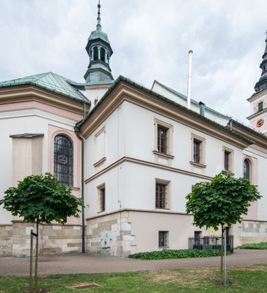 Zdjęcie nr 27: Kościół orientowany, murowany, trzynawowy. Typ halowy, z węższym, prostokątnym prezbiterium zamkniętym trójbocznie oraz z wieżą wbudowaną w zachodnią fasadę. Do prezbiterium od północy przylega zakrystia (do niej od zachodu klatka schodowa wiodąca do skarbca na piętrze), od południa natomiast kaplica Morsztynów z XVII wieku. Kaplica na planie prostokąta zamkniętego trójbocznie, z niszami w ściętych narożach, pod nią sklepiona krypta grobowa, opięta pilastrami wewnątrz i na zewnątrz. Od południa do korpusu przylega kruchta stanowiąca również kaplicę Matki Boskiej Pocieszenia. Korpus czteroprzęsłowy, nawy oddzielają arkady wsparte na filarach, pierwsze stanowią podparcie dla chóru. Nad nawami i prezbiterium strop imitujący sklepienie, na którym malowana dekoracja imitująca gurty, plafony oraz stiuki. Dekoracja ścian powtarza podziały wyznaczone przez arkady, namalowano na nich pilastry podtrzymujące belkowanie. W prezbiterium dwa okna usytuowane niedaleko ołtarza, w nawie osiem, wszystkie w kształcie stojącego prostokąta zamkniętego półkoliście, wypełnione witrażami z dekoracją geometryczną. Główne wejście od zachodu, drugie od północy, trzecie symetrycznie od południa przez kruchtę sklepioną kopułą, kolejne trzy do prezbiterium, od południa przez zakrystię i od północy przez kruchtę. 
Fasada zachodnia na cokole, podzielona gzymsami i lizenami, z wieżą zakończoną hełmem. Na osi drzwi w kształcie stojącego prostokąta flankowane prostokątnymi oknami, powyżej trzecie, większe okno zamknięte łukiem odcinkowym; kondygnację wieńczy gzyms. Druga kondygnacja powtarza podziały pierwszej. W środkowej osi okulus, powyżej dwudzielne okno zamknięte półkoliście. Nad nim tarcza zegara, kolejne dwie na ścianach bocznych. Kondygnacja ograniczona po bokach spływali wolutowymi i obeliskami zakończonymi kulami; przechodzi w wieżę. Powyżej gzyms podtrzymywany kroksztynami. Ostatnia kondygnacja o artykulacji ramowej z balkonami z każdej strony, powyżej wieńczącego gzymsu. Pozostałe elewacje na cokole, kontynuują podziały  lizenowo-ramowe, artykulacją podkreślają okna. Kaplica Morsztynów opięta pilastrami z głowicami, prezbiterium oszkarpowane. Dach nad nawą główną, kaplicą i prezbiterium dwuspadowy, na kruchtą południową kopuła, na wieży ozdobny hełm dołem wklęsły, dekorowany wolutami. Powyżej kopuła, na której latarnia przepruta arkadami i zwieńczona przewężoną w środku kopułą zakończoną ostrosłupem z kulą i krzyżem. 
Do najcenniejszych zabytków świątyni należą m.in. zaprojektowana przez Jana Delamarsa kaplica Morsztynów dekorowana stiukami z 1693 roku autorstwa Baltazara Fontany. Wewnątrz niej warto zwrócić uwagę na osiemnastowieczny ołtarz z przedstawieniem Oblicza Chrystusa i rzeźbionym antepedium. W ołtarz Ukrzyżowania znajdujący się w północnej nawie kościoła wkomponowano gotyckie rzeźby św. Jana i Marii. 