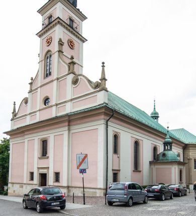 Zdjęcie nr 1: Kościół orientowany, murowany, trzynawowy. Typ halowy, z węższym, prostokątnym prezbiterium zamkniętym trójbocznie oraz z wieżą wbudowaną w zachodnią fasadę. Do prezbiterium od północy przylega zakrystia (do niej od zachodu klatka schodowa wiodąca do skarbca na piętrze), od południa natomiast kaplica Morsztynów z XVII wieku. Kaplica na planie prostokąta zamkniętego trójbocznie, z niszami w ściętych narożach, pod nią sklepiona krypta grobowa, opięta pilastrami wewnątrz i na zewnątrz. Od południa do korpusu przylega kruchta stanowiąca również kaplicę Matki Boskiej Pocieszenia. Korpus czteroprzęsłowy, nawy oddzielają arkady wsparte na filarach, pierwsze stanowią podparcie dla chóru. Nad nawami i prezbiterium strop imitujący sklepienie, na którym malowana dekoracja imitująca gurty, plafony oraz stiuki. Dekoracja ścian powtarza podziały wyznaczone przez arkady, namalowano na nich pilastry podtrzymujące belkowanie. W prezbiterium dwa okna usytuowane niedaleko ołtarza, w nawie osiem, wszystkie w kształcie stojącego prostokąta zamkniętego półkoliście, wypełnione witrażami z dekoracją geometryczną. Główne wejście od zachodu, drugie od północy, trzecie symetrycznie od południa przez kruchtę sklepioną kopułą, kolejne trzy do prezbiterium, od południa przez zakrystię i od północy przez kruchtę. 
Fasada zachodnia na cokole, podzielona gzymsami i lizenami, z wieżą zakończoną hełmem. Na osi drzwi w kształcie stojącego prostokąta flankowane prostokątnymi oknami, powyżej trzecie, większe okno zamknięte łukiem odcinkowym; kondygnację wieńczy gzyms. Druga kondygnacja powtarza podziały pierwszej. W środkowej osi okulus, powyżej dwudzielne okno zamknięte półkoliście. Nad nim tarcza zegara, kolejne dwie na ścianach bocznych. Kondygnacja ograniczona po bokach spływali wolutowymi i obeliskami zakończonymi kulami; przechodzi w wieżę. Powyżej gzyms podtrzymywany kroksztynami. Ostatnia kondygnacja o artykulacji ramowej z balkonami z każdej strony, powyżej wieńczącego gzymsu. Pozostałe elewacje na cokole, kontynuują podziały  lizenowo-ramowe, artykulacją podkreślają okna. Kaplica Morsztynów opięta pilastrami z głowicami, prezbiterium oszkarpowane. Dach nad nawą główną, kaplicą i prezbiterium dwuspadowy, na kruchtą południową kopuła, na wieży ozdobny hełm dołem wklęsły, dekorowany wolutami. Powyżej kopuła, na której latarnia przepruta arkadami i zwieńczona przewężoną w środku kopułą zakończoną ostrosłupem z kulą i krzyżem. 
Do najcenniejszych zabytków świątyni należą m.in. zaprojektowana przez Jana Delamarsa kaplica Morsztynów dekorowana stiukami z 1693 roku autorstwa Baltazara Fontany. Wewnątrz niej warto zwrócić uwagę na osiemnastowieczny ołtarz z przedstawieniem Oblicza Chrystusa i rzeźbionym antepedium. W ołtarz Ukrzyżowania znajdujący się w północnej nawie kościoła wkomponowano gotyckie rzeźby św. Jana i Marii. 