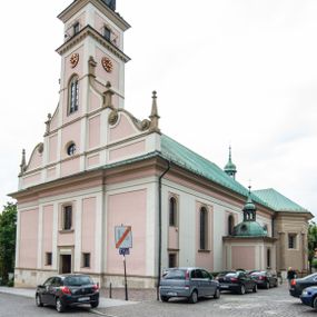 Zdjęcie nr 1: Kościół orientowany, murowany, trzynawowy. Typ halowy, z węższym, prostokątnym prezbiterium zamkniętym trójbocznie oraz z wieżą wbudowaną w zachodnią fasadę. Do prezbiterium od północy przylega zakrystia (do niej od zachodu klatka schodowa wiodąca do skarbca na piętrze), od południa natomiast kaplica Morsztynów z XVII wieku. Kaplica na planie prostokąta zamkniętego trójbocznie, z niszami w ściętych narożach, pod nią sklepiona krypta grobowa, opięta pilastrami wewnątrz i na zewnątrz. Od południa do korpusu przylega kruchta stanowiąca również kaplicę Matki Boskiej Pocieszenia. Korpus czteroprzęsłowy, nawy oddzielają arkady wsparte na filarach, pierwsze stanowią podparcie dla chóru. Nad nawami i prezbiterium strop imitujący sklepienie, na którym malowana dekoracja imitująca gurty, plafony oraz stiuki. Dekoracja ścian powtarza podziały wyznaczone przez arkady, namalowano na nich pilastry podtrzymujące belkowanie. W prezbiterium dwa okna usytuowane niedaleko ołtarza, w nawie osiem, wszystkie w kształcie stojącego prostokąta zamkniętego półkoliście, wypełnione witrażami z dekoracją geometryczną. Główne wejście od zachodu, drugie od północy, trzecie symetrycznie od południa przez kruchtę sklepioną kopułą, kolejne trzy do prezbiterium, od południa przez zakrystię i od północy przez kruchtę. 
Fasada zachodnia na cokole, podzielona gzymsami i lizenami, z wieżą zakończoną hełmem. Na osi drzwi w kształcie stojącego prostokąta flankowane prostokątnymi oknami, powyżej trzecie, większe okno zamknięte łukiem odcinkowym; kondygnację wieńczy gzyms. Druga kondygnacja powtarza podziały pierwszej. W środkowej osi okulus, powyżej dwudzielne okno zamknięte półkoliście. Nad nim tarcza zegara, kolejne dwie na ścianach bocznych. Kondygnacja ograniczona po bokach spływali wolutowymi i obeliskami zakończonymi kulami; przechodzi w wieżę. Powyżej gzyms podtrzymywany kroksztynami. Ostatnia kondygnacja o artykulacji ramowej z balkonami z każdej strony, powyżej wieńczącego gzymsu. Pozostałe elewacje na cokole, kontynuują podziały  lizenowo-ramowe, artykulacją podkreślają okna. Kaplica Morsztynów opięta pilastrami z głowicami, prezbiterium oszkarpowane. Dach nad nawą główną, kaplicą i prezbiterium dwuspadowy, na kruchtą południową kopuła, na wieży ozdobny hełm dołem wklęsły, dekorowany wolutami. Powyżej kopuła, na której latarnia przepruta arkadami i zwieńczona przewężoną w środku kopułą zakończoną ostrosłupem z kulą i krzyżem. 
Do najcenniejszych zabytków świątyni należą m.in. zaprojektowana przez Jana Delamarsa kaplica Morsztynów dekorowana stiukami z 1693 roku autorstwa Baltazara Fontany. Wewnątrz niej warto zwrócić uwagę na osiemnastowieczny ołtarz z przedstawieniem Oblicza Chrystusa i rzeźbionym antepedium. W ołtarz Ukrzyżowania znajdujący się w północnej nawie kościoła wkomponowano gotyckie rzeźby św. Jana i Marii. 