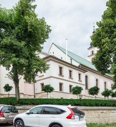 Zdjęcie nr 46: Kościół orientowany, murowany, trzynawowy. Typ halowy, z węższym, prostokątnym prezbiterium zamkniętym trójbocznie oraz z wieżą wbudowaną w zachodnią fasadę. Do prezbiterium od północy przylega zakrystia (do niej od zachodu klatka schodowa wiodąca do skarbca na piętrze), od południa natomiast kaplica Morsztynów z XVII wieku. Kaplica na planie prostokąta zamkniętego trójbocznie, z niszami w ściętych narożach, pod nią sklepiona krypta grobowa, opięta pilastrami wewnątrz i na zewnątrz. Od południa do korpusu przylega kruchta stanowiąca również kaplicę Matki Boskiej Pocieszenia. Korpus czteroprzęsłowy, nawy oddzielają arkady wsparte na filarach, pierwsze stanowią podparcie dla chóru. Nad nawami i prezbiterium strop imitujący sklepienie, na którym malowana dekoracja imitująca gurty, plafony oraz stiuki. Dekoracja ścian powtarza podziały wyznaczone przez arkady, namalowano na nich pilastry podtrzymujące belkowanie. W prezbiterium dwa okna usytuowane niedaleko ołtarza, w nawie osiem, wszystkie w kształcie stojącego prostokąta zamkniętego półkoliście, wypełnione witrażami z dekoracją geometryczną. Główne wejście od zachodu, drugie od północy, trzecie symetrycznie od południa przez kruchtę sklepioną kopułą, kolejne trzy do prezbiterium, od południa przez zakrystię i od północy przez kruchtę. 
Fasada zachodnia na cokole, podzielona gzymsami i lizenami, z wieżą zakończoną hełmem. Na osi drzwi w kształcie stojącego prostokąta flankowane prostokątnymi oknami, powyżej trzecie, większe okno zamknięte łukiem odcinkowym; kondygnację wieńczy gzyms. Druga kondygnacja powtarza podziały pierwszej. W środkowej osi okulus, powyżej dwudzielne okno zamknięte półkoliście. Nad nim tarcza zegara, kolejne dwie na ścianach bocznych. Kondygnacja ograniczona po bokach spływali wolutowymi i obeliskami zakończonymi kulami; przechodzi w wieżę. Powyżej gzyms podtrzymywany kroksztynami. Ostatnia kondygnacja o artykulacji ramowej z balkonami z każdej strony, powyżej wieńczącego gzymsu. Pozostałe elewacje na cokole, kontynuują podziały  lizenowo-ramowe, artykulacją podkreślają okna. Kaplica Morsztynów opięta pilastrami z głowicami, prezbiterium oszkarpowane. Dach nad nawą główną, kaplicą i prezbiterium dwuspadowy, na kruchtą południową kopuła, na wieży ozdobny hełm dołem wklęsły, dekorowany wolutami. Powyżej kopuła, na której latarnia przepruta arkadami i zwieńczona przewężoną w środku kopułą zakończoną ostrosłupem z kulą i krzyżem. 
Do najcenniejszych zabytków świątyni należą m.in. zaprojektowana przez Jana Delamarsa kaplica Morsztynów dekorowana stiukami z 1693 roku autorstwa Baltazara Fontany. Wewnątrz niej warto zwrócić uwagę na osiemnastowieczny ołtarz z przedstawieniem Oblicza Chrystusa i rzeźbionym antepedium. W ołtarz Ukrzyżowania znajdujący się w północnej nawie kościoła wkomponowano gotyckie rzeźby św. Jana i Marii. 