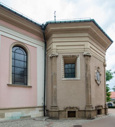 Zdjęcie nr 23: Kościół orientowany, murowany, trzynawowy. Typ halowy, z węższym, prostokątnym prezbiterium zamkniętym trójbocznie oraz z wieżą wbudowaną w zachodnią fasadę. Do prezbiterium od północy przylega zakrystia (do niej od zachodu klatka schodowa wiodąca do skarbca na piętrze), od południa natomiast kaplica Morsztynów z XVII wieku. Kaplica na planie prostokąta zamkniętego trójbocznie, z niszami w ściętych narożach, pod nią sklepiona krypta grobowa, opięta pilastrami wewnątrz i na zewnątrz. Od południa do korpusu przylega kruchta stanowiąca również kaplicę Matki Boskiej Pocieszenia. Korpus czteroprzęsłowy, nawy oddzielają arkady wsparte na filarach, pierwsze stanowią podparcie dla chóru. Nad nawami i prezbiterium strop imitujący sklepienie, na którym malowana dekoracja imitująca gurty, plafony oraz stiuki. Dekoracja ścian powtarza podziały wyznaczone przez arkady, namalowano na nich pilastry podtrzymujące belkowanie. W prezbiterium dwa okna usytuowane niedaleko ołtarza, w nawie osiem, wszystkie w kształcie stojącego prostokąta zamkniętego półkoliście, wypełnione witrażami z dekoracją geometryczną. Główne wejście od zachodu, drugie od północy, trzecie symetrycznie od południa przez kruchtę sklepioną kopułą, kolejne trzy do prezbiterium, od południa przez zakrystię i od północy przez kruchtę. 
Fasada zachodnia na cokole, podzielona gzymsami i lizenami, z wieżą zakończoną hełmem. Na osi drzwi w kształcie stojącego prostokąta flankowane prostokątnymi oknami, powyżej trzecie, większe okno zamknięte łukiem odcinkowym; kondygnację wieńczy gzyms. Druga kondygnacja powtarza podziały pierwszej. W środkowej osi okulus, powyżej dwudzielne okno zamknięte półkoliście. Nad nim tarcza zegara, kolejne dwie na ścianach bocznych. Kondygnacja ograniczona po bokach spływali wolutowymi i obeliskami zakończonymi kulami; przechodzi w wieżę. Powyżej gzyms podtrzymywany kroksztynami. Ostatnia kondygnacja o artykulacji ramowej z balkonami z każdej strony, powyżej wieńczącego gzymsu. Pozostałe elewacje na cokole, kontynuują podziały  lizenowo-ramowe, artykulacją podkreślają okna. Kaplica Morsztynów opięta pilastrami z głowicami, prezbiterium oszkarpowane. Dach nad nawą główną, kaplicą i prezbiterium dwuspadowy, na kruchtą południową kopuła, na wieży ozdobny hełm dołem wklęsły, dekorowany wolutami. Powyżej kopuła, na której latarnia przepruta arkadami i zwieńczona przewężoną w środku kopułą zakończoną ostrosłupem z kulą i krzyżem. 
Do najcenniejszych zabytków świątyni należą m.in. zaprojektowana przez Jana Delamarsa kaplica Morsztynów dekorowana stiukami z 1693 roku autorstwa Baltazara Fontany. Wewnątrz niej warto zwrócić uwagę na osiemnastowieczny ołtarz z przedstawieniem Oblicza Chrystusa i rzeźbionym antepedium. W ołtarz Ukrzyżowania znajdujący się w północnej nawie kościoła wkomponowano gotyckie rzeźby św. Jana i Marii. 