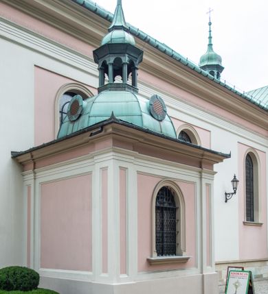 Zdjęcie nr 31: Kościół orientowany, murowany, trzynawowy. Typ halowy, z węższym, prostokątnym prezbiterium zamkniętym trójbocznie oraz z wieżą wbudowaną w zachodnią fasadę. Do prezbiterium od północy przylega zakrystia (do niej od zachodu klatka schodowa wiodąca do skarbca na piętrze), od południa natomiast kaplica Morsztynów z XVII wieku. Kaplica na planie prostokąta zamkniętego trójbocznie, z niszami w ściętych narożach, pod nią sklepiona krypta grobowa, opięta pilastrami wewnątrz i na zewnątrz. Od południa do korpusu przylega kruchta stanowiąca również kaplicę Matki Boskiej Pocieszenia. Korpus czteroprzęsłowy, nawy oddzielają arkady wsparte na filarach, pierwsze stanowią podparcie dla chóru. Nad nawami i prezbiterium strop imitujący sklepienie, na którym malowana dekoracja imitująca gurty, plafony oraz stiuki. Dekoracja ścian powtarza podziały wyznaczone przez arkady, namalowano na nich pilastry podtrzymujące belkowanie. W prezbiterium dwa okna usytuowane niedaleko ołtarza, w nawie osiem, wszystkie w kształcie stojącego prostokąta zamkniętego półkoliście, wypełnione witrażami z dekoracją geometryczną. Główne wejście od zachodu, drugie od północy, trzecie symetrycznie od południa przez kruchtę sklepioną kopułą, kolejne trzy do prezbiterium, od południa przez zakrystię i od północy przez kruchtę. 
Fasada zachodnia na cokole, podzielona gzymsami i lizenami, z wieżą zakończoną hełmem. Na osi drzwi w kształcie stojącego prostokąta flankowane prostokątnymi oknami, powyżej trzecie, większe okno zamknięte łukiem odcinkowym; kondygnację wieńczy gzyms. Druga kondygnacja powtarza podziały pierwszej. W środkowej osi okulus, powyżej dwudzielne okno zamknięte półkoliście. Nad nim tarcza zegara, kolejne dwie na ścianach bocznych. Kondygnacja ograniczona po bokach spływali wolutowymi i obeliskami zakończonymi kulami; przechodzi w wieżę. Powyżej gzyms podtrzymywany kroksztynami. Ostatnia kondygnacja o artykulacji ramowej z balkonami z każdej strony, powyżej wieńczącego gzymsu. Pozostałe elewacje na cokole, kontynuują podziały  lizenowo-ramowe, artykulacją podkreślają okna. Kaplica Morsztynów opięta pilastrami z głowicami, prezbiterium oszkarpowane. Dach nad nawą główną, kaplicą i prezbiterium dwuspadowy, na kruchtą południową kopuła, na wieży ozdobny hełm dołem wklęsły, dekorowany wolutami. Powyżej kopuła, na której latarnia przepruta arkadami i zwieńczona przewężoną w środku kopułą zakończoną ostrosłupem z kulą i krzyżem. 
Do najcenniejszych zabytków świątyni należą m.in. zaprojektowana przez Jana Delamarsa kaplica Morsztynów dekorowana stiukami z 1693 roku autorstwa Baltazara Fontany. Wewnątrz niej warto zwrócić uwagę na osiemnastowieczny ołtarz z przedstawieniem Oblicza Chrystusa i rzeźbionym antepedium. W ołtarz Ukrzyżowania znajdujący się w północnej nawie kościoła wkomponowano gotyckie rzeźby św. Jana i Marii. 