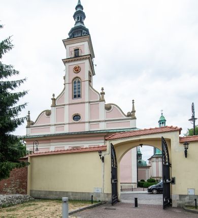 Zdjęcie nr 9: Kościół orientowany, murowany, trzynawowy. Typ halowy, z węższym, prostokątnym prezbiterium zamkniętym trójbocznie oraz z wieżą wbudowaną w zachodnią fasadę. Do prezbiterium od północy przylega zakrystia (do niej od zachodu klatka schodowa wiodąca do skarbca na piętrze), od południa natomiast kaplica Morsztynów z XVII wieku. Kaplica na planie prostokąta zamkniętego trójbocznie, z niszami w ściętych narożach, pod nią sklepiona krypta grobowa, opięta pilastrami wewnątrz i na zewnątrz. Od południa do korpusu przylega kruchta stanowiąca również kaplicę Matki Boskiej Pocieszenia. Korpus czteroprzęsłowy, nawy oddzielają arkady wsparte na filarach, pierwsze stanowią podparcie dla chóru. Nad nawami i prezbiterium strop imitujący sklepienie, na którym malowana dekoracja imitująca gurty, plafony oraz stiuki. Dekoracja ścian powtarza podziały wyznaczone przez arkady, namalowano na nich pilastry podtrzymujące belkowanie. W prezbiterium dwa okna usytuowane niedaleko ołtarza, w nawie osiem, wszystkie w kształcie stojącego prostokąta zamkniętego półkoliście, wypełnione witrażami z dekoracją geometryczną. Główne wejście od zachodu, drugie od północy, trzecie symetrycznie od południa przez kruchtę sklepioną kopułą, kolejne trzy do prezbiterium, od południa przez zakrystię i od północy przez kruchtę. 
Fasada zachodnia na cokole, podzielona gzymsami i lizenami, z wieżą zakończoną hełmem. Na osi drzwi w kształcie stojącego prostokąta flankowane prostokątnymi oknami, powyżej trzecie, większe okno zamknięte łukiem odcinkowym; kondygnację wieńczy gzyms. Druga kondygnacja powtarza podziały pierwszej. W środkowej osi okulus, powyżej dwudzielne okno zamknięte półkoliście. Nad nim tarcza zegara, kolejne dwie na ścianach bocznych. Kondygnacja ograniczona po bokach spływali wolutowymi i obeliskami zakończonymi kulami; przechodzi w wieżę. Powyżej gzyms podtrzymywany kroksztynami. Ostatnia kondygnacja o artykulacji ramowej z balkonami z każdej strony, powyżej wieńczącego gzymsu. Pozostałe elewacje na cokole, kontynuują podziały  lizenowo-ramowe, artykulacją podkreślają okna. Kaplica Morsztynów opięta pilastrami z głowicami, prezbiterium oszkarpowane. Dach nad nawą główną, kaplicą i prezbiterium dwuspadowy, na kruchtą południową kopuła, na wieży ozdobny hełm dołem wklęsły, dekorowany wolutami. Powyżej kopuła, na której latarnia przepruta arkadami i zwieńczona przewężoną w środku kopułą zakończoną ostrosłupem z kulą i krzyżem. 
Do najcenniejszych zabytków świątyni należą m.in. zaprojektowana przez Jana Delamarsa kaplica Morsztynów dekorowana stiukami z 1693 roku autorstwa Baltazara Fontany. Wewnątrz niej warto zwrócić uwagę na osiemnastowieczny ołtarz z przedstawieniem Oblicza Chrystusa i rzeźbionym antepedium. W ołtarz Ukrzyżowania znajdujący się w północnej nawie kościoła wkomponowano gotyckie rzeźby św. Jana i Marii. 