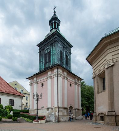 Zdjęcie nr 36: Kościół orientowany, murowany, trzynawowy. Typ halowy, z węższym, prostokątnym prezbiterium zamkniętym trójbocznie oraz z wieżą wbudowaną w zachodnią fasadę. Do prezbiterium od północy przylega zakrystia (do niej od zachodu klatka schodowa wiodąca do skarbca na piętrze), od południa natomiast kaplica Morsztynów z XVII wieku. Kaplica na planie prostokąta zamkniętego trójbocznie, z niszami w ściętych narożach, pod nią sklepiona krypta grobowa, opięta pilastrami wewnątrz i na zewnątrz. Od południa do korpusu przylega kruchta stanowiąca również kaplicę Matki Boskiej Pocieszenia. Korpus czteroprzęsłowy, nawy oddzielają arkady wsparte na filarach, pierwsze stanowią podparcie dla chóru. Nad nawami i prezbiterium strop imitujący sklepienie, na którym malowana dekoracja imitująca gurty, plafony oraz stiuki. Dekoracja ścian powtarza podziały wyznaczone przez arkady, namalowano na nich pilastry podtrzymujące belkowanie. W prezbiterium dwa okna usytuowane niedaleko ołtarza, w nawie osiem, wszystkie w kształcie stojącego prostokąta zamkniętego półkoliście, wypełnione witrażami z dekoracją geometryczną. Główne wejście od zachodu, drugie od północy, trzecie symetrycznie od południa przez kruchtę sklepioną kopułą, kolejne trzy do prezbiterium, od południa przez zakrystię i od północy przez kruchtę. 
Fasada zachodnia na cokole, podzielona gzymsami i lizenami, z wieżą zakończoną hełmem. Na osi drzwi w kształcie stojącego prostokąta flankowane prostokątnymi oknami, powyżej trzecie, większe okno zamknięte łukiem odcinkowym; kondygnację wieńczy gzyms. Druga kondygnacja powtarza podziały pierwszej. W środkowej osi okulus, powyżej dwudzielne okno zamknięte półkoliście. Nad nim tarcza zegara, kolejne dwie na ścianach bocznych. Kondygnacja ograniczona po bokach spływali wolutowymi i obeliskami zakończonymi kulami; przechodzi w wieżę. Powyżej gzyms podtrzymywany kroksztynami. Ostatnia kondygnacja o artykulacji ramowej z balkonami z każdej strony, powyżej wieńczącego gzymsu. Pozostałe elewacje na cokole, kontynuują podziały  lizenowo-ramowe, artykulacją podkreślają okna. Kaplica Morsztynów opięta pilastrami z głowicami, prezbiterium oszkarpowane. Dach nad nawą główną, kaplicą i prezbiterium dwuspadowy, na kruchtą południową kopuła, na wieży ozdobny hełm dołem wklęsły, dekorowany wolutami. Powyżej kopuła, na której latarnia przepruta arkadami i zwieńczona przewężoną w środku kopułą zakończoną ostrosłupem z kulą i krzyżem. 
Do najcenniejszych zabytków świątyni należą m.in. zaprojektowana przez Jana Delamarsa kaplica Morsztynów dekorowana stiukami z 1693 roku autorstwa Baltazara Fontany. Wewnątrz niej warto zwrócić uwagę na osiemnastowieczny ołtarz z przedstawieniem Oblicza Chrystusa i rzeźbionym antepedium. W ołtarz Ukrzyżowania znajdujący się w północnej nawie kościoła wkomponowano gotyckie rzeźby św. Jana i Marii. 