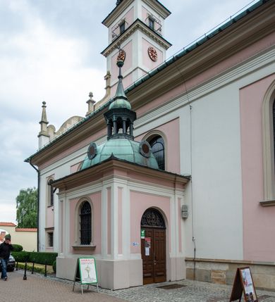 Zdjęcie nr 30: Kościół orientowany, murowany, trzynawowy. Typ halowy, z węższym, prostokątnym prezbiterium zamkniętym trójbocznie oraz z wieżą wbudowaną w zachodnią fasadę. Do prezbiterium od północy przylega zakrystia (do niej od zachodu klatka schodowa wiodąca do skarbca na piętrze), od południa natomiast kaplica Morsztynów z XVII wieku. Kaplica na planie prostokąta zamkniętego trójbocznie, z niszami w ściętych narożach, pod nią sklepiona krypta grobowa, opięta pilastrami wewnątrz i na zewnątrz. Od południa do korpusu przylega kruchta stanowiąca również kaplicę Matki Boskiej Pocieszenia. Korpus czteroprzęsłowy, nawy oddzielają arkady wsparte na filarach, pierwsze stanowią podparcie dla chóru. Nad nawami i prezbiterium strop imitujący sklepienie, na którym malowana dekoracja imitująca gurty, plafony oraz stiuki. Dekoracja ścian powtarza podziały wyznaczone przez arkady, namalowano na nich pilastry podtrzymujące belkowanie. W prezbiterium dwa okna usytuowane niedaleko ołtarza, w nawie osiem, wszystkie w kształcie stojącego prostokąta zamkniętego półkoliście, wypełnione witrażami z dekoracją geometryczną. Główne wejście od zachodu, drugie od północy, trzecie symetrycznie od południa przez kruchtę sklepioną kopułą, kolejne trzy do prezbiterium, od południa przez zakrystię i od północy przez kruchtę. 
Fasada zachodnia na cokole, podzielona gzymsami i lizenami, z wieżą zakończoną hełmem. Na osi drzwi w kształcie stojącego prostokąta flankowane prostokątnymi oknami, powyżej trzecie, większe okno zamknięte łukiem odcinkowym; kondygnację wieńczy gzyms. Druga kondygnacja powtarza podziały pierwszej. W środkowej osi okulus, powyżej dwudzielne okno zamknięte półkoliście. Nad nim tarcza zegara, kolejne dwie na ścianach bocznych. Kondygnacja ograniczona po bokach spływali wolutowymi i obeliskami zakończonymi kulami; przechodzi w wieżę. Powyżej gzyms podtrzymywany kroksztynami. Ostatnia kondygnacja o artykulacji ramowej z balkonami z każdej strony, powyżej wieńczącego gzymsu. Pozostałe elewacje na cokole, kontynuują podziały  lizenowo-ramowe, artykulacją podkreślają okna. Kaplica Morsztynów opięta pilastrami z głowicami, prezbiterium oszkarpowane. Dach nad nawą główną, kaplicą i prezbiterium dwuspadowy, na kruchtą południową kopuła, na wieży ozdobny hełm dołem wklęsły, dekorowany wolutami. Powyżej kopuła, na której latarnia przepruta arkadami i zwieńczona przewężoną w środku kopułą zakończoną ostrosłupem z kulą i krzyżem. 
Do najcenniejszych zabytków świątyni należą m.in. zaprojektowana przez Jana Delamarsa kaplica Morsztynów dekorowana stiukami z 1693 roku autorstwa Baltazara Fontany. Wewnątrz niej warto zwrócić uwagę na osiemnastowieczny ołtarz z przedstawieniem Oblicza Chrystusa i rzeźbionym antepedium. W ołtarz Ukrzyżowania znajdujący się w północnej nawie kościoła wkomponowano gotyckie rzeźby św. Jana i Marii. 