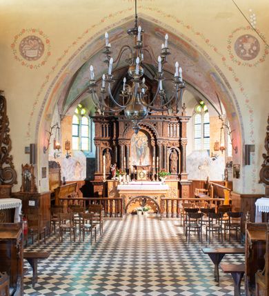 Zdjęcie nr 9: Kościół orientowany, jest budowlą murowaną z kamienia, na rzucie podłużnym. Korpus jednonawowy i dwuprzęsłowy. Do stosunkowo szerokiego, jednoprzęsłowego, zamkniętego trójbocznie prezbiterium od północy przylega zakrystia, a na osi kościoła, od zachodu kruchta. Prezbiterium przekryte jest sklepieniem krzyżowo-żebrowym, a nawa drewnianym sklepieniem kolebkowymi.  Przestrzeń prezbiterium od korpusu nawowego oddziela ostrołukowa arkada tęczowa i drewniana balustrada. Artykulację ścian na zewnątrz kościoła stanowi wieniec przypór ujmujących ściany i naroża korpusu nawowego i prezbiterium.  Do wnętrza prowadzą trzy otwory drzwiowe – jeden przez kruchtę w elewacji północnej, jeden w północnej ścianie korpusu nawowego i jeden przez zakrystię. Dwuskrzydłowe drzwi w kruchcie ujęte są portalem zamkniętym łukiem dwuramiennym, portale pozostałych otworów drzwiowych są ostrołukowe. Ściany korpusu nawowego i prezbiterium przeprute są smukłymi, ostrołukowymi oknami, w nawie wypełnionymi gomółkami, a w prezbiterium dekoracją maswerkową. W szczycie fasady para małych, wąskich okienek w kształcie stojących prostokątów, analogiczne w szczycie kruchty. Korpus nawowy, prezbiterium i zakrystia przekryte są jednym dachem dwuspadowym, wykonanym z blachy, kruchta także dachem dwuspadowym. Na połączeniu nawy i prezbiterium umieszczona jest wieżyczka na sygnaturkę, także obita blachą. Kolorystyka tynków kościoła utrzymana jest w kolorze białym, fasada i kruchta są kamienne. 