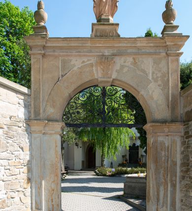 Zdjęcie nr 5: Kościół orientowany, jest budowlą murowaną z kamienia, na rzucie podłużnym. Korpus jednonawowy i dwuprzęsłowy. Do stosunkowo szerokiego, jednoprzęsłowego, zamkniętego trójbocznie prezbiterium od północy przylega zakrystia, a na osi kościoła, od zachodu kruchta. Prezbiterium przekryte jest sklepieniem krzyżowo-żebrowym, a nawa drewnianym sklepieniem kolebkowymi.  Przestrzeń prezbiterium od korpusu nawowego oddziela ostrołukowa arkada tęczowa i drewniana balustrada. Artykulację ścian na zewnątrz kościoła stanowi wieniec przypór ujmujących ściany i naroża korpusu nawowego i prezbiterium.  Do wnętrza prowadzą trzy otwory drzwiowe – jeden przez kruchtę w elewacji północnej, jeden w północnej ścianie korpusu nawowego i jeden przez zakrystię. Dwuskrzydłowe drzwi w kruchcie ujęte są portalem zamkniętym łukiem dwuramiennym, portale pozostałych otworów drzwiowych są ostrołukowe. Ściany korpusu nawowego i prezbiterium przeprute są smukłymi, ostrołukowymi oknami, w nawie wypełnionymi gomółkami, a w prezbiterium dekoracją maswerkową. W szczycie fasady para małych, wąskich okienek w kształcie stojących prostokątów, analogiczne w szczycie kruchty. Korpus nawowy, prezbiterium i zakrystia przekryte są jednym dachem dwuspadowym, wykonanym z blachy, kruchta także dachem dwuspadowym. Na połączeniu nawy i prezbiterium umieszczona jest wieżyczka na sygnaturkę, także obita blachą. Kolorystyka tynków kościoła utrzymana jest w kolorze białym, fasada i kruchta są kamienne. 