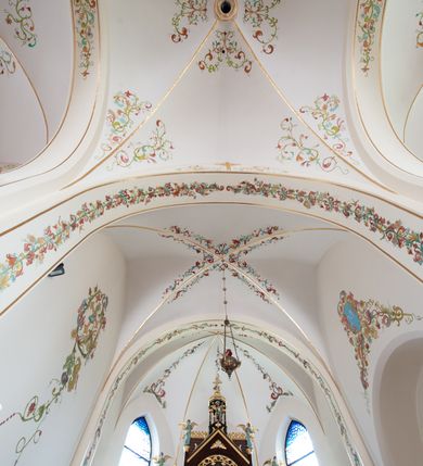 Zdjęcie nr 4: Kościół jest położony w centrum wsi, na północ od główne drogi we wsi, na placu otoczonym kamiennym murem, nakrytym betonowym daszkiem, obsadzony ozdobnym drzewostanem. Wejście na plac kościelny prowadzi przez bramę od południa i wąską furtkę od zachodu. Kościół jest budowlą założoną na planie krzyża łacińskiego, murowaną, skierowaną na północ, trójnawową z transeptem i prezbiterium zakończonym wielobocznie. Wewnątrz dwuprzęsłowe nawy oddzielone są ostrołukowymi arkadami wspartymi na zdwojonych filarach oraz na parze kolumn pośrodku świątyni. Podpory wspierają sklepienie krzyżowo-żebrowe. Od fasady dostawiona masywna wieża na planie prostokąta, zwężająca się ku górze, nakryta namiotowym daszkiem i zwieńczona krzyżem. Wejście południowe w formie prostokątnego portalu, ujętego w dużą ostrołukową arkadę wykonaną z kamiennej okładziny. Powyżej na tle trójdzielnego okna ustawiona jest figura Chrystusa. Pomiędzy zachodnim ramieniem transeptu, a prezbiterium dostawiona zakrystia z wejściem od północy, analogicznie po drugiej stronie kościoła kaplica Najświętszego Serca Pana Jezusa. Nad skrzyżowaniem ramion transeptu umieszczona jest ażurowa wieżyczka na sygnaturkę. Całość opięta szkarpami. Detale dekoracyjne, takie jak narożniki, portale, gzymsy i obramowania okien wykonane z piaskowca. Do świątyni prowadzi też zachodni przedsionek.