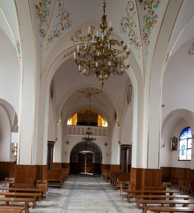 Zdjęcie nr 14: Kościół jest położony w centrum wsi, na północ od główne drogi we wsi, na placu otoczonym kamiennym murem, nakrytym betonowym daszkiem, obsadzony ozdobnym drzewostanem. Wejście na plac kościelny prowadzi przez bramę od południa i wąską furtkę od zachodu. Kościół jest budowlą założoną na planie krzyża łacińskiego, murowaną, skierowaną na północ, trójnawową z transeptem i prezbiterium zakończonym wielobocznie. Wewnątrz dwuprzęsłowe nawy oddzielone są ostrołukowymi arkadami wspartymi na zdwojonych filarach oraz na parze kolumn pośrodku świątyni. Podpory wspierają sklepienie krzyżowo-żebrowe. Od fasady dostawiona masywna wieża na planie prostokąta, zwężająca się ku górze, nakryta namiotowym daszkiem i zwieńczona krzyżem. Wejście południowe w formie prostokątnego portalu, ujętego w dużą ostrołukową arkadę wykonaną z kamiennej okładziny. Powyżej na tle trójdzielnego okna ustawiona jest figura Chrystusa. Pomiędzy zachodnim ramieniem transeptu, a prezbiterium dostawiona zakrystia z wejściem od północy, analogicznie po drugiej stronie kościoła kaplica Najświętszego Serca Pana Jezusa. Nad skrzyżowaniem ramion transeptu umieszczona jest ażurowa wieżyczka na sygnaturkę. Całość opięta szkarpami. Detale dekoracyjne, takie jak narożniki, portale, gzymsy i obramowania okien wykonane z piaskowca. Do świątyni prowadzi też zachodni przedsionek.