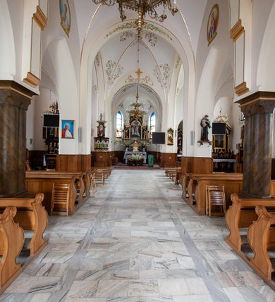 Zdjęcie nr 9: Kościół jest położony w centrum wsi, na północ od główne drogi we wsi, na placu otoczonym kamiennym murem, nakrytym betonowym daszkiem, obsadzony ozdobnym drzewostanem. Wejście na plac kościelny prowadzi przez bramę od południa i wąską furtkę od zachodu. Kościół jest budowlą założoną na planie krzyża łacińskiego, murowaną, skierowaną na północ, trójnawową z transeptem i prezbiterium zakończonym wielobocznie. Wewnątrz dwuprzęsłowe nawy oddzielone są ostrołukowymi arkadami wspartymi na zdwojonych filarach oraz na parze kolumn pośrodku świątyni. Podpory wspierają sklepienie krzyżowo-żebrowe. Od fasady dostawiona masywna wieża na planie prostokąta, zwężająca się ku górze, nakryta namiotowym daszkiem i zwieńczona krzyżem. Wejście południowe w formie prostokątnego portalu, ujętego w dużą ostrołukową arkadę wykonaną z kamiennej okładziny. Powyżej na tle trójdzielnego okna ustawiona jest figura Chrystusa. Pomiędzy zachodnim ramieniem transeptu, a prezbiterium dostawiona zakrystia z wejściem od północy, analogicznie po drugiej stronie kościoła kaplica Najświętszego Serca Pana Jezusa. Nad skrzyżowaniem ramion transeptu umieszczona jest ażurowa wieżyczka na sygnaturkę. Całość opięta szkarpami. Detale dekoracyjne, takie jak narożniki, portale, gzymsy i obramowania okien wykonane z piaskowca. Do świątyni prowadzi też zachodni przedsionek.