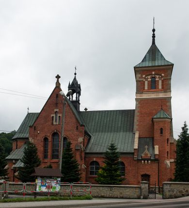 Zdjęcie nr 2: Kościół jest położony w centrum wsi, na północ od główne drogi we wsi, na placu otoczonym kamiennym murem, nakrytym betonowym daszkiem, obsadzony ozdobnym drzewostanem. Wejście na plac kościelny prowadzi przez bramę od południa i wąską furtkę od zachodu. Kościół jest budowlą założoną na planie krzyża łacińskiego, murowaną, skierowaną na północ, trójnawową z transeptem i prezbiterium zakończonym wielobocznie. Wewnątrz dwuprzęsłowe nawy oddzielone są ostrołukowymi arkadami wspartymi na zdwojonych filarach oraz na parze kolumn pośrodku świątyni. Podpory wspierają sklepienie krzyżowo-żebrowe. Od fasady dostawiona masywna wieża na planie prostokąta, zwężająca się ku górze, nakryta namiotowym daszkiem i zwieńczona krzyżem. Wejście południowe w formie prostokątnego portalu, ujętego w dużą ostrołukową arkadę wykonaną z kamiennej okładziny. Powyżej na tle trójdzielnego okna ustawiona jest figura Chrystusa. Pomiędzy zachodnim ramieniem transeptu, a prezbiterium dostawiona zakrystia z wejściem od północy, analogicznie po drugiej stronie kościoła kaplica Najświętszego Serca Pana Jezusa. Nad skrzyżowaniem ramion transeptu umieszczona jest ażurowa wieżyczka na sygnaturkę. Całość opięta szkarpami. Detale dekoracyjne, takie jak narożniki, portale, gzymsy i obramowania okien wykonane z piaskowca. Do świątyni prowadzi też zachodni przedsionek.
