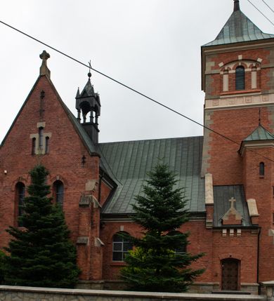 Zdjęcie nr 7: Kościół jest położony w centrum wsi, na północ od główne drogi we wsi, na placu otoczonym kamiennym murem, nakrytym betonowym daszkiem, obsadzony ozdobnym drzewostanem. Wejście na plac kościelny prowadzi przez bramę od południa i wąską furtkę od zachodu. Kościół jest budowlą założoną na planie krzyża łacińskiego, murowaną, skierowaną na północ, trójnawową z transeptem i prezbiterium zakończonym wielobocznie. Wewnątrz dwuprzęsłowe nawy oddzielone są ostrołukowymi arkadami wspartymi na zdwojonych filarach oraz na parze kolumn pośrodku świątyni. Podpory wspierają sklepienie krzyżowo-żebrowe. Od fasady dostawiona masywna wieża na planie prostokąta, zwężająca się ku górze, nakryta namiotowym daszkiem i zwieńczona krzyżem. Wejście południowe w formie prostokątnego portalu, ujętego w dużą ostrołukową arkadę wykonaną z kamiennej okładziny. Powyżej na tle trójdzielnego okna ustawiona jest figura Chrystusa. Pomiędzy zachodnim ramieniem transeptu, a prezbiterium dostawiona zakrystia z wejściem od północy, analogicznie po drugiej stronie kościoła kaplica Najświętszego Serca Pana Jezusa. Nad skrzyżowaniem ramion transeptu umieszczona jest ażurowa wieżyczka na sygnaturkę. Całość opięta szkarpami. Detale dekoracyjne, takie jak narożniki, portale, gzymsy i obramowania okien wykonane z piaskowca. Do świątyni prowadzi też zachodni przedsionek.