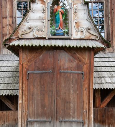 Zdjęcie nr 59: Kościół drewniany, orientowany, składający się z babińca, nawy głównej z przylegającą do niej od północy kaplicą boczną i kruchtą od południa oraz prezbiterium z zakrystią od północy. Prezbiterium i nawa w konstrukcji zrębowej, wieża, soboty i kruchta w słupowej. Kościół jednonawowy, nawa prawie kwadratowa, prezbiterium prostokątne, zamknięte prosto, oddzielone ścianą tęczową. Otwór tęczowy zamknięty łukiem dwuramiennym z biegnącą w poprzek grubą belką. Ściany gładkie, pokryte dekoracją malarską imitującą poziomo ułożone belki z uszczelniającymi je kiczkami, scenami figuralnymi, zacheuszkami i pasami ornamentalnymi. W nawie od zachodu chór muzyczny wsparty na dwóch, profilowanych słupach, z parapetem wybrzuszonym pośrodku; z dekoracją malarską o motywach geometryczno-roślinnych. Nawa i prezbiterium naryte pozornym sklepieniem z pułapami lekko zaokrąglonymi po bokach. Na całości przekrycia dekoracja malarska. W prezbiterium są to postacie aniołów wśród stylizowanych kwiatów na stropie adorujących monogram maryjny, nawę dekorują motywy roślinne. Anioły zdobią również sklepienie kaplicy. Strop babińca oraz fragmenty prezbiterium pokrywa oryginalna dekoracja patronowa złożona z motywów geometrycznych oraz figuralnych. W nawie głównej trzy okna, w prezbiterium i babińcu po dwa – od południa, kolejne do zakrystii; zamknięte łukiem dwuspadowym. Główne wejście od zachodu, drugie przez kruchtę od południa, trzecie do zakrystii. Portal południowy ostrołukowy, dekorowany ornamentem sznurowym, portal do zakrystii zamknięty łukiem w ośli grzbiet. Od zachodu kwadratowa wieża o pochyłych ścianach, z nadwieszoną izbicą, zwieńczona czteropołaciowym, ostrosłupowym hełmem gontowym. Izbica wieży oszalowana dookoła deskami zakończonymi u dołu ozdobnie wyrzynaną koronką. Od południa i wschodu soboty, czyli rodzaj podcieni,  w pozostałych miejscach gontowy kołnierz. Ściany świątyni oraz kaplicy są od zewnątrz szalowane deskami, wieża oraz przedsionek obite są gontem. Dachy i zadaszenia sobot pokryte gontem, kopuła kaplicy oraz wieżyczka na sygnaturkę pokryta blachą. 