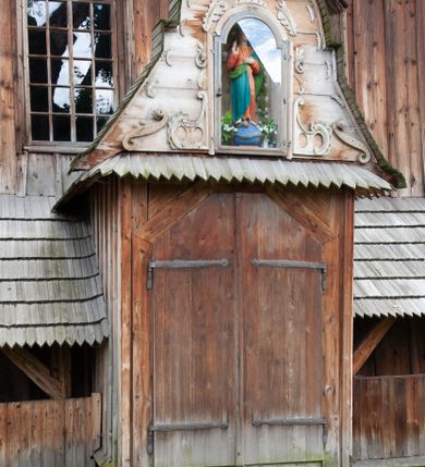 Zdjęcie nr 58: Kościół drewniany, orientowany, składający się z babińca, nawy głównej z przylegającą do niej od północy kaplicą boczną i kruchtą od południa oraz prezbiterium z zakrystią od północy. Prezbiterium i nawa w konstrukcji zrębowej, wieża, soboty i kruchta w słupowej. Kościół jednonawowy, nawa prawie kwadratowa, prezbiterium prostokątne, zamknięte prosto, oddzielone ścianą tęczową. Otwór tęczowy zamknięty łukiem dwuramiennym z biegnącą w poprzek grubą belką. Ściany gładkie, pokryte dekoracją malarską imitującą poziomo ułożone belki z uszczelniającymi je kiczkami, scenami figuralnymi, zacheuszkami i pasami ornamentalnymi. W nawie od zachodu chór muzyczny wsparty na dwóch, profilowanych słupach, z parapetem wybrzuszonym pośrodku; z dekoracją malarską o motywach geometryczno-roślinnych. Nawa i prezbiterium naryte pozornym sklepieniem z pułapami lekko zaokrąglonymi po bokach. Na całości przekrycia dekoracja malarska. W prezbiterium są to postacie aniołów wśród stylizowanych kwiatów na stropie adorujących monogram maryjny, nawę dekorują motywy roślinne. Anioły zdobią również sklepienie kaplicy. Strop babińca oraz fragmenty prezbiterium pokrywa oryginalna dekoracja patronowa złożona z motywów geometrycznych oraz figuralnych. W nawie głównej trzy okna, w prezbiterium i babińcu po dwa – od południa, kolejne do zakrystii; zamknięte łukiem dwuspadowym. Główne wejście od zachodu, drugie przez kruchtę od południa, trzecie do zakrystii. Portal południowy ostrołukowy, dekorowany ornamentem sznurowym, portal do zakrystii zamknięty łukiem w ośli grzbiet. Od zachodu kwadratowa wieża o pochyłych ścianach, z nadwieszoną izbicą, zwieńczona czteropołaciowym, ostrosłupowym hełmem gontowym. Izbica wieży oszalowana dookoła deskami zakończonymi u dołu ozdobnie wyrzynaną koronką. Od południa i wschodu soboty, czyli rodzaj podcieni,  w pozostałych miejscach gontowy kołnierz. Ściany świątyni oraz kaplicy są od zewnątrz szalowane deskami, wieża oraz przedsionek obite są gontem. Dachy i zadaszenia sobot pokryte gontem, kopuła kaplicy oraz wieżyczka na sygnaturkę pokryta blachą. 