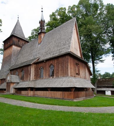 Zdjęcie nr 50: Kościół drewniany, orientowany, składający się z babińca, nawy głównej z przylegającą do niej od północy kaplicą boczną i kruchtą od południa oraz prezbiterium z zakrystią od północy. Prezbiterium i nawa w konstrukcji zrębowej, wieża, soboty i kruchta w słupowej. Kościół jednonawowy, nawa prawie kwadratowa, prezbiterium prostokątne, zamknięte prosto, oddzielone ścianą tęczową. Otwór tęczowy zamknięty łukiem dwuramiennym z biegnącą w poprzek grubą belką. Ściany gładkie, pokryte dekoracją malarską imitującą poziomo ułożone belki z uszczelniającymi je kiczkami, scenami figuralnymi, zacheuszkami i pasami ornamentalnymi. W nawie od zachodu chór muzyczny wsparty na dwóch, profilowanych słupach, z parapetem wybrzuszonym pośrodku; z dekoracją malarską o motywach geometryczno-roślinnych. Nawa i prezbiterium naryte pozornym sklepieniem z pułapami lekko zaokrąglonymi po bokach. Na całości przekrycia dekoracja malarska. W prezbiterium są to postacie aniołów wśród stylizowanych kwiatów na stropie adorujących monogram maryjny, nawę dekorują motywy roślinne. Anioły zdobią również sklepienie kaplicy. Strop babińca oraz fragmenty prezbiterium pokrywa oryginalna dekoracja patronowa złożona z motywów geometrycznych oraz figuralnych. W nawie głównej trzy okna, w prezbiterium i babińcu po dwa – od południa, kolejne do zakrystii; zamknięte łukiem dwuspadowym. Główne wejście od zachodu, drugie przez kruchtę od południa, trzecie do zakrystii. Portal południowy ostrołukowy, dekorowany ornamentem sznurowym, portal do zakrystii zamknięty łukiem w ośli grzbiet. Od zachodu kwadratowa wieża o pochyłych ścianach, z nadwieszoną izbicą, zwieńczona czteropołaciowym, ostrosłupowym hełmem gontowym. Izbica wieży oszalowana dookoła deskami zakończonymi u dołu ozdobnie wyrzynaną koronką. Od południa i wschodu soboty, czyli rodzaj podcieni,  w pozostałych miejscach gontowy kołnierz. Ściany świątyni oraz kaplicy są od zewnątrz szalowane deskami, wieża oraz przedsionek obite są gontem. Dachy i zadaszenia sobot pokryte gontem, kopuła kaplicy oraz wieżyczka na sygnaturkę pokryta blachą. 