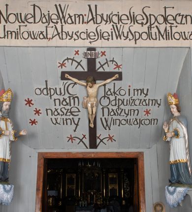 Zdjęcie nr 26: Kościół drewniany, orientowany, składający się z babińca, nawy głównej z przylegającą do niej od północy kaplicą boczną i kruchtą od południa oraz prezbiterium z zakrystią od północy. Prezbiterium i nawa w konstrukcji zrębowej, wieża, soboty i kruchta w słupowej. Kościół jednonawowy, nawa prawie kwadratowa, prezbiterium prostokątne, zamknięte prosto, oddzielone ścianą tęczową. Otwór tęczowy zamknięty łukiem dwuramiennym z biegnącą w poprzek grubą belką. Ściany gładkie, pokryte dekoracją malarską imitującą poziomo ułożone belki z uszczelniającymi je kiczkami, scenami figuralnymi, zacheuszkami i pasami ornamentalnymi. W nawie od zachodu chór muzyczny wsparty na dwóch, profilowanych słupach, z parapetem wybrzuszonym pośrodku; z dekoracją malarską o motywach geometryczno-roślinnych. Nawa i prezbiterium naryte pozornym sklepieniem z pułapami lekko zaokrąglonymi po bokach. Na całości przekrycia dekoracja malarska. W prezbiterium są to postacie aniołów wśród stylizowanych kwiatów na stropie adorujących monogram maryjny, nawę dekorują motywy roślinne. Anioły zdobią również sklepienie kaplicy. Strop babińca oraz fragmenty prezbiterium pokrywa oryginalna dekoracja patronowa złożona z motywów geometrycznych oraz figuralnych. W nawie głównej trzy okna, w prezbiterium i babińcu po dwa – od południa, kolejne do zakrystii; zamknięte łukiem dwuspadowym. Główne wejście od zachodu, drugie przez kruchtę od południa, trzecie do zakrystii. Portal południowy ostrołukowy, dekorowany ornamentem sznurowym, portal do zakrystii zamknięty łukiem w ośli grzbiet. Od zachodu kwadratowa wieża o pochyłych ścianach, z nadwieszoną izbicą, zwieńczona czteropołaciowym, ostrosłupowym hełmem gontowym. Izbica wieży oszalowana dookoła deskami zakończonymi u dołu ozdobnie wyrzynaną koronką. Od południa i wschodu soboty, czyli rodzaj podcieni,  w pozostałych miejscach gontowy kołnierz. Ściany świątyni oraz kaplicy są od zewnątrz szalowane deskami, wieża oraz przedsionek obite są gontem. Dachy i zadaszenia sobot pokryte gontem, kopuła kaplicy oraz wieżyczka na sygnaturkę pokryta blachą. 