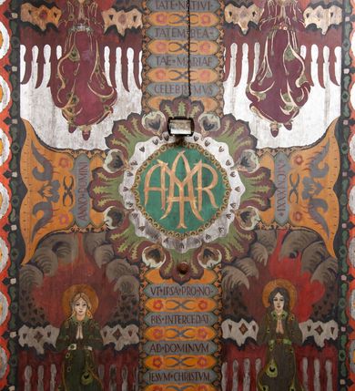 Zdjęcie nr 12: Kościół drewniany, orientowany, składający się z babińca, nawy głównej z przylegającą do niej od północy kaplicą boczną i kruchtą od południa oraz prezbiterium z zakrystią od północy. Prezbiterium i nawa w konstrukcji zrębowej, wieża, soboty i kruchta w słupowej. Kościół jednonawowy, nawa prawie kwadratowa, prezbiterium prostokątne, zamknięte prosto, oddzielone ścianą tęczową. Otwór tęczowy zamknięty łukiem dwuramiennym z biegnącą w poprzek grubą belką. Ściany gładkie, pokryte dekoracją malarską imitującą poziomo ułożone belki z uszczelniającymi je kiczkami, scenami figuralnymi, zacheuszkami i pasami ornamentalnymi. W nawie od zachodu chór muzyczny wsparty na dwóch, profilowanych słupach, z parapetem wybrzuszonym pośrodku; z dekoracją malarską o motywach geometryczno-roślinnych. Nawa i prezbiterium naryte pozornym sklepieniem z pułapami lekko zaokrąglonymi po bokach. Na całości przekrycia dekoracja malarska. W prezbiterium są to postacie aniołów wśród stylizowanych kwiatów na stropie adorujących monogram maryjny, nawę dekorują motywy roślinne. Anioły zdobią również sklepienie kaplicy. Strop babińca oraz fragmenty prezbiterium pokrywa oryginalna dekoracja patronowa złożona z motywów geometrycznych oraz figuralnych. W nawie głównej trzy okna, w prezbiterium i babińcu po dwa – od południa, kolejne do zakrystii; zamknięte łukiem dwuspadowym. Główne wejście od zachodu, drugie przez kruchtę od południa, trzecie do zakrystii. Portal południowy ostrołukowy, dekorowany ornamentem sznurowym, portal do zakrystii zamknięty łukiem w ośli grzbiet. Od zachodu kwadratowa wieża o pochyłych ścianach, z nadwieszoną izbicą, zwieńczona czteropołaciowym, ostrosłupowym hełmem gontowym. Izbica wieży oszalowana dookoła deskami zakończonymi u dołu ozdobnie wyrzynaną koronką. Od południa i wschodu soboty, czyli rodzaj podcieni,  w pozostałych miejscach gontowy kołnierz. Ściany świątyni oraz kaplicy są od zewnątrz szalowane deskami, wieża oraz przedsionek obite są gontem. Dachy i zadaszenia sobot pokryte gontem, kopuła kaplicy oraz wieżyczka na sygnaturkę pokryta blachą. 