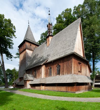 Zdjęcie nr 51: Kościół drewniany, orientowany, składający się z babińca, nawy głównej z przylegającą do niej od północy kaplicą boczną i kruchtą od południa oraz prezbiterium z zakrystią od północy. Prezbiterium i nawa w konstrukcji zrębowej, wieża, soboty i kruchta w słupowej. Kościół jednonawowy, nawa prawie kwadratowa, prezbiterium prostokątne, zamknięte prosto, oddzielone ścianą tęczową. Otwór tęczowy zamknięty łukiem dwuramiennym z biegnącą w poprzek grubą belką. Ściany gładkie, pokryte dekoracją malarską imitującą poziomo ułożone belki z uszczelniającymi je kiczkami, scenami figuralnymi, zacheuszkami i pasami ornamentalnymi. W nawie od zachodu chór muzyczny wsparty na dwóch, profilowanych słupach, z parapetem wybrzuszonym pośrodku; z dekoracją malarską o motywach geometryczno-roślinnych. Nawa i prezbiterium naryte pozornym sklepieniem z pułapami lekko zaokrąglonymi po bokach. Na całości przekrycia dekoracja malarska. W prezbiterium są to postacie aniołów wśród stylizowanych kwiatów na stropie adorujących monogram maryjny, nawę dekorują motywy roślinne. Anioły zdobią również sklepienie kaplicy. Strop babińca oraz fragmenty prezbiterium pokrywa oryginalna dekoracja patronowa złożona z motywów geometrycznych oraz figuralnych. W nawie głównej trzy okna, w prezbiterium i babińcu po dwa – od południa, kolejne do zakrystii; zamknięte łukiem dwuspadowym. Główne wejście od zachodu, drugie przez kruchtę od południa, trzecie do zakrystii. Portal południowy ostrołukowy, dekorowany ornamentem sznurowym, portal do zakrystii zamknięty łukiem w ośli grzbiet. Od zachodu kwadratowa wieża o pochyłych ścianach, z nadwieszoną izbicą, zwieńczona czteropołaciowym, ostrosłupowym hełmem gontowym. Izbica wieży oszalowana dookoła deskami zakończonymi u dołu ozdobnie wyrzynaną koronką. Od południa i wschodu soboty, czyli rodzaj podcieni,  w pozostałych miejscach gontowy kołnierz. Ściany świątyni oraz kaplicy są od zewnątrz szalowane deskami, wieża oraz przedsionek obite są gontem. Dachy i zadaszenia sobot pokryte gontem, kopuła kaplicy oraz wieżyczka na sygnaturkę pokryta blachą. 