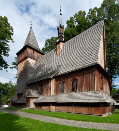 Zdjęcie nr 52: Kościół drewniany, orientowany, składający się z babińca, nawy głównej z przylegającą do niej od północy kaplicą boczną i kruchtą od południa oraz prezbiterium z zakrystią od północy. Prezbiterium i nawa w konstrukcji zrębowej, wieża, soboty i kruchta w słupowej. Kościół jednonawowy, nawa prawie kwadratowa, prezbiterium prostokątne, zamknięte prosto, oddzielone ścianą tęczową. Otwór tęczowy zamknięty łukiem dwuramiennym z biegnącą w poprzek grubą belką. Ściany gładkie, pokryte dekoracją malarską imitującą poziomo ułożone belki z uszczelniającymi je kiczkami, scenami figuralnymi, zacheuszkami i pasami ornamentalnymi. W nawie od zachodu chór muzyczny wsparty na dwóch, profilowanych słupach, z parapetem wybrzuszonym pośrodku; z dekoracją malarską o motywach geometryczno-roślinnych. Nawa i prezbiterium naryte pozornym sklepieniem z pułapami lekko zaokrąglonymi po bokach. Na całości przekrycia dekoracja malarska. W prezbiterium są to postacie aniołów wśród stylizowanych kwiatów na stropie adorujących monogram maryjny, nawę dekorują motywy roślinne. Anioły zdobią również sklepienie kaplicy. Strop babińca oraz fragmenty prezbiterium pokrywa oryginalna dekoracja patronowa złożona z motywów geometrycznych oraz figuralnych. W nawie głównej trzy okna, w prezbiterium i babińcu po dwa – od południa, kolejne do zakrystii; zamknięte łukiem dwuspadowym. Główne wejście od zachodu, drugie przez kruchtę od południa, trzecie do zakrystii. Portal południowy ostrołukowy, dekorowany ornamentem sznurowym, portal do zakrystii zamknięty łukiem w ośli grzbiet. Od zachodu kwadratowa wieża o pochyłych ścianach, z nadwieszoną izbicą, zwieńczona czteropołaciowym, ostrosłupowym hełmem gontowym. Izbica wieży oszalowana dookoła deskami zakończonymi u dołu ozdobnie wyrzynaną koronką. Od południa i wschodu soboty, czyli rodzaj podcieni,  w pozostałych miejscach gontowy kołnierz. Ściany świątyni oraz kaplicy są od zewnątrz szalowane deskami, wieża oraz przedsionek obite są gontem. Dachy i zadaszenia sobot pokryte gontem, kopuła kaplicy oraz wieżyczka na sygnaturkę pokryta blachą. 