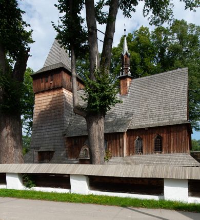 Zdjęcie nr 46: Kościół drewniany, orientowany, składający się z babińca, nawy głównej z przylegającą do niej od północy kaplicą boczną i kruchtą od południa oraz prezbiterium z zakrystią od północy. Prezbiterium i nawa w konstrukcji zrębowej, wieża, soboty i kruchta w słupowej. Kościół jednonawowy, nawa prawie kwadratowa, prezbiterium prostokątne, zamknięte prosto, oddzielone ścianą tęczową. Otwór tęczowy zamknięty łukiem dwuramiennym z biegnącą w poprzek grubą belką. Ściany gładkie, pokryte dekoracją malarską imitującą poziomo ułożone belki z uszczelniającymi je kiczkami, scenami figuralnymi, zacheuszkami i pasami ornamentalnymi. W nawie od zachodu chór muzyczny wsparty na dwóch, profilowanych słupach, z parapetem wybrzuszonym pośrodku; z dekoracją malarską o motywach geometryczno-roślinnych. Nawa i prezbiterium naryte pozornym sklepieniem z pułapami lekko zaokrąglonymi po bokach. Na całości przekrycia dekoracja malarska. W prezbiterium są to postacie aniołów wśród stylizowanych kwiatów na stropie adorujących monogram maryjny, nawę dekorują motywy roślinne. Anioły zdobią również sklepienie kaplicy. Strop babińca oraz fragmenty prezbiterium pokrywa oryginalna dekoracja patronowa złożona z motywów geometrycznych oraz figuralnych. W nawie głównej trzy okna, w prezbiterium i babińcu po dwa – od południa, kolejne do zakrystii; zamknięte łukiem dwuspadowym. Główne wejście od zachodu, drugie przez kruchtę od południa, trzecie do zakrystii. Portal południowy ostrołukowy, dekorowany ornamentem sznurowym, portal do zakrystii zamknięty łukiem w ośli grzbiet. Od zachodu kwadratowa wieża o pochyłych ścianach, z nadwieszoną izbicą, zwieńczona czteropołaciowym, ostrosłupowym hełmem gontowym. Izbica wieży oszalowana dookoła deskami zakończonymi u dołu ozdobnie wyrzynaną koronką. Od południa i wschodu soboty, czyli rodzaj podcieni,  w pozostałych miejscach gontowy kołnierz. Ściany świątyni oraz kaplicy są od zewnątrz szalowane deskami, wieża oraz przedsionek obite są gontem. Dachy i zadaszenia sobot pokryte gontem, kopuła kaplicy oraz wieżyczka na sygnaturkę pokryta blachą. 