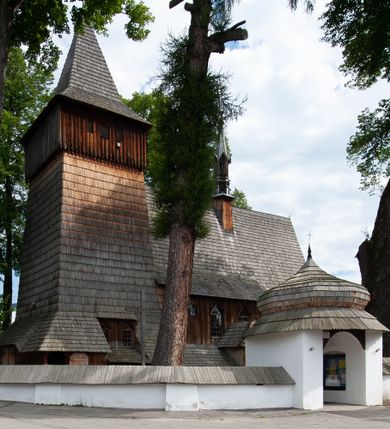 Zdjęcie nr 1: Kościół drewniany, orientowany, składający się z babińca, nawy głównej z przylegającą do niej od północy kaplicą boczną i kruchtą od południa oraz prezbiterium z zakrystią od północy. Prezbiterium i nawa w konstrukcji zrębowej, wieża, soboty i kruchta w słupowej. Kościół jednonawowy, nawa prawie kwadratowa, prezbiterium prostokątne, zamknięte prosto, oddzielone ścianą tęczową. Otwór tęczowy zamknięty łukiem dwuramiennym z biegnącą w poprzek grubą belką. Ściany gładkie, pokryte dekoracją malarską imitującą poziomo ułożone belki z uszczelniającymi je kiczkami, scenami figuralnymi, zacheuszkami i pasami ornamentalnymi. W nawie od zachodu chór muzyczny wsparty na dwóch, profilowanych słupach, z parapetem wybrzuszonym pośrodku; z dekoracją malarską o motywach geometryczno-roślinnych. Nawa i prezbiterium naryte pozornym sklepieniem z pułapami lekko zaokrąglonymi po bokach. Na całości przekrycia dekoracja malarska. W prezbiterium są to postacie aniołów wśród stylizowanych kwiatów na stropie adorujących monogram maryjny, nawę dekorują motywy roślinne. Anioły zdobią również sklepienie kaplicy. Strop babińca oraz fragmenty prezbiterium pokrywa oryginalna dekoracja patronowa złożona z motywów geometrycznych oraz figuralnych. W nawie głównej trzy okna, w prezbiterium i babińcu po dwa – od południa, kolejne do zakrystii; zamknięte łukiem dwuspadowym. Główne wejście od zachodu, drugie przez kruchtę od południa, trzecie do zakrystii. Portal południowy ostrołukowy, dekorowany ornamentem sznurowym, portal do zakrystii zamknięty łukiem w ośli grzbiet. Od zachodu kwadratowa wieża o pochyłych ścianach, z nadwieszoną izbicą, zwieńczona czteropołaciowym, ostrosłupowym hełmem gontowym. Izbica wieży oszalowana dookoła deskami zakończonymi u dołu ozdobnie wyrzynaną koronką. Od południa i wschodu soboty, czyli rodzaj podcieni,  w pozostałych miejscach gontowy kołnierz. Ściany świątyni oraz kaplicy są od zewnątrz szalowane deskami, wieża oraz przedsionek obite są gontem. Dachy i zadaszenia sobot pokryte gontem, kopuła kaplicy oraz wieżyczka na sygnaturkę pokryta blachą. 