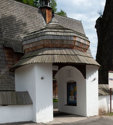 Zdjęcie nr 5: Kościół drewniany, orientowany, składający się z babińca, nawy głównej z przylegającą do niej od północy kaplicą boczną i kruchtą od południa oraz prezbiterium z zakrystią od północy. Prezbiterium i nawa w konstrukcji zrębowej, wieża, soboty i kruchta w słupowej. Kościół jednonawowy, nawa prawie kwadratowa, prezbiterium prostokątne, zamknięte prosto, oddzielone ścianą tęczową. Otwór tęczowy zamknięty łukiem dwuramiennym z biegnącą w poprzek grubą belką. Ściany gładkie, pokryte dekoracją malarską imitującą poziomo ułożone belki z uszczelniającymi je kiczkami, scenami figuralnymi, zacheuszkami i pasami ornamentalnymi. W nawie od zachodu chór muzyczny wsparty na dwóch, profilowanych słupach, z parapetem wybrzuszonym pośrodku; z dekoracją malarską o motywach geometryczno-roślinnych. Nawa i prezbiterium naryte pozornym sklepieniem z pułapami lekko zaokrąglonymi po bokach. Na całości przekrycia dekoracja malarska. W prezbiterium są to postacie aniołów wśród stylizowanych kwiatów na stropie adorujących monogram maryjny, nawę dekorują motywy roślinne. Anioły zdobią również sklepienie kaplicy. Strop babińca oraz fragmenty prezbiterium pokrywa oryginalna dekoracja patronowa złożona z motywów geometrycznych oraz figuralnych. W nawie głównej trzy okna, w prezbiterium i babińcu po dwa – od południa, kolejne do zakrystii; zamknięte łukiem dwuspadowym. Główne wejście od zachodu, drugie przez kruchtę od południa, trzecie do zakrystii. Portal południowy ostrołukowy, dekorowany ornamentem sznurowym, portal do zakrystii zamknięty łukiem w ośli grzbiet. Od zachodu kwadratowa wieża o pochyłych ścianach, z nadwieszoną izbicą, zwieńczona czteropołaciowym, ostrosłupowym hełmem gontowym. Izbica wieży oszalowana dookoła deskami zakończonymi u dołu ozdobnie wyrzynaną koronką. Od południa i wschodu soboty, czyli rodzaj podcieni,  w pozostałych miejscach gontowy kołnierz. Ściany świątyni oraz kaplicy są od zewnątrz szalowane deskami, wieża oraz przedsionek obite są gontem. Dachy i zadaszenia sobot pokryte gontem, kopuła kaplicy oraz wieżyczka na sygnaturkę pokryta blachą. 