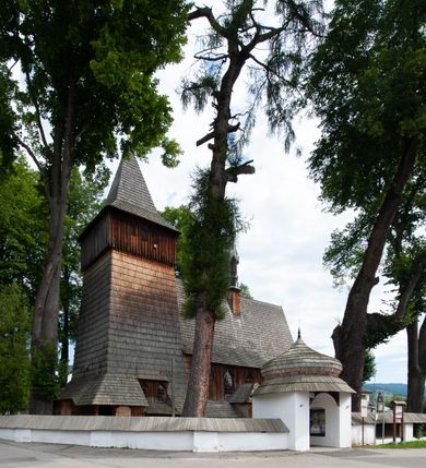 Zdjęcie nr 42: Kościół drewniany, orientowany, składający się z babińca, nawy głównej z przylegającą do niej od północy kaplicą boczną i kruchtą od południa oraz prezbiterium z zakrystią od północy. Prezbiterium i nawa w konstrukcji zrębowej, wieża, soboty i kruchta w słupowej. Kościół jednonawowy, nawa prawie kwadratowa, prezbiterium prostokątne, zamknięte prosto, oddzielone ścianą tęczową. Otwór tęczowy zamknięty łukiem dwuramiennym z biegnącą w poprzek grubą belką. Ściany gładkie, pokryte dekoracją malarską imitującą poziomo ułożone belki z uszczelniającymi je kiczkami, scenami figuralnymi, zacheuszkami i pasami ornamentalnymi. W nawie od zachodu chór muzyczny wsparty na dwóch, profilowanych słupach, z parapetem wybrzuszonym pośrodku; z dekoracją malarską o motywach geometryczno-roślinnych. Nawa i prezbiterium naryte pozornym sklepieniem z pułapami lekko zaokrąglonymi po bokach. Na całości przekrycia dekoracja malarska. W prezbiterium są to postacie aniołów wśród stylizowanych kwiatów na stropie adorujących monogram maryjny, nawę dekorują motywy roślinne. Anioły zdobią również sklepienie kaplicy. Strop babińca oraz fragmenty prezbiterium pokrywa oryginalna dekoracja patronowa złożona z motywów geometrycznych oraz figuralnych. W nawie głównej trzy okna, w prezbiterium i babińcu po dwa – od południa, kolejne do zakrystii; zamknięte łukiem dwuspadowym. Główne wejście od zachodu, drugie przez kruchtę od południa, trzecie do zakrystii. Portal południowy ostrołukowy, dekorowany ornamentem sznurowym, portal do zakrystii zamknięty łukiem w ośli grzbiet. Od zachodu kwadratowa wieża o pochyłych ścianach, z nadwieszoną izbicą, zwieńczona czteropołaciowym, ostrosłupowym hełmem gontowym. Izbica wieży oszalowana dookoła deskami zakończonymi u dołu ozdobnie wyrzynaną koronką. Od południa i wschodu soboty, czyli rodzaj podcieni,  w pozostałych miejscach gontowy kołnierz. Ściany świątyni oraz kaplicy są od zewnątrz szalowane deskami, wieża oraz przedsionek obite są gontem. Dachy i zadaszenia sobot pokryte gontem, kopuła kaplicy oraz wieżyczka na sygnaturkę pokryta blachą. 