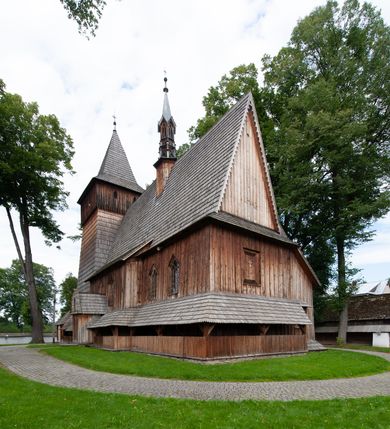 Zdjęcie nr 49: Kościół drewniany, orientowany, składający się z babińca, nawy głównej z przylegającą do niej od północy kaplicą boczną i kruchtą od południa oraz prezbiterium z zakrystią od północy. Prezbiterium i nawa w konstrukcji zrębowej, wieża, soboty i kruchta w słupowej. Kościół jednonawowy, nawa prawie kwadratowa, prezbiterium prostokątne, zamknięte prosto, oddzielone ścianą tęczową. Otwór tęczowy zamknięty łukiem dwuramiennym z biegnącą w poprzek grubą belką. Ściany gładkie, pokryte dekoracją malarską imitującą poziomo ułożone belki z uszczelniającymi je kiczkami, scenami figuralnymi, zacheuszkami i pasami ornamentalnymi. W nawie od zachodu chór muzyczny wsparty na dwóch, profilowanych słupach, z parapetem wybrzuszonym pośrodku; z dekoracją malarską o motywach geometryczno-roślinnych. Nawa i prezbiterium naryte pozornym sklepieniem z pułapami lekko zaokrąglonymi po bokach. Na całości przekrycia dekoracja malarska. W prezbiterium są to postacie aniołów wśród stylizowanych kwiatów na stropie adorujących monogram maryjny, nawę dekorują motywy roślinne. Anioły zdobią również sklepienie kaplicy. Strop babińca oraz fragmenty prezbiterium pokrywa oryginalna dekoracja patronowa złożona z motywów geometrycznych oraz figuralnych. W nawie głównej trzy okna, w prezbiterium i babińcu po dwa – od południa, kolejne do zakrystii; zamknięte łukiem dwuspadowym. Główne wejście od zachodu, drugie przez kruchtę od południa, trzecie do zakrystii. Portal południowy ostrołukowy, dekorowany ornamentem sznurowym, portal do zakrystii zamknięty łukiem w ośli grzbiet. Od zachodu kwadratowa wieża o pochyłych ścianach, z nadwieszoną izbicą, zwieńczona czteropołaciowym, ostrosłupowym hełmem gontowym. Izbica wieży oszalowana dookoła deskami zakończonymi u dołu ozdobnie wyrzynaną koronką. Od południa i wschodu soboty, czyli rodzaj podcieni,  w pozostałych miejscach gontowy kołnierz. Ściany świątyni oraz kaplicy są od zewnątrz szalowane deskami, wieża oraz przedsionek obite są gontem. Dachy i zadaszenia sobot pokryte gontem, kopuła kaplicy oraz wieżyczka na sygnaturkę pokryta blachą. 