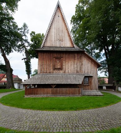 Zdjęcie nr 61: Kościół drewniany, orientowany, składający się z babińca, nawy głównej z przylegającą do niej od północy kaplicą boczną i kruchtą od południa oraz prezbiterium z zakrystią od północy. Prezbiterium i nawa w konstrukcji zrębowej, wieża, soboty i kruchta w słupowej. Kościół jednonawowy, nawa prawie kwadratowa, prezbiterium prostokątne, zamknięte prosto, oddzielone ścianą tęczową. Otwór tęczowy zamknięty łukiem dwuramiennym z biegnącą w poprzek grubą belką. Ściany gładkie, pokryte dekoracją malarską imitującą poziomo ułożone belki z uszczelniającymi je kiczkami, scenami figuralnymi, zacheuszkami i pasami ornamentalnymi. W nawie od zachodu chór muzyczny wsparty na dwóch, profilowanych słupach, z parapetem wybrzuszonym pośrodku; z dekoracją malarską o motywach geometryczno-roślinnych. Nawa i prezbiterium naryte pozornym sklepieniem z pułapami lekko zaokrąglonymi po bokach. Na całości przekrycia dekoracja malarska. W prezbiterium są to postacie aniołów wśród stylizowanych kwiatów na stropie adorujących monogram maryjny, nawę dekorują motywy roślinne. Anioły zdobią również sklepienie kaplicy. Strop babińca oraz fragmenty prezbiterium pokrywa oryginalna dekoracja patronowa złożona z motywów geometrycznych oraz figuralnych. W nawie głównej trzy okna, w prezbiterium i babińcu po dwa – od południa, kolejne do zakrystii; zamknięte łukiem dwuspadowym. Główne wejście od zachodu, drugie przez kruchtę od południa, trzecie do zakrystii. Portal południowy ostrołukowy, dekorowany ornamentem sznurowym, portal do zakrystii zamknięty łukiem w ośli grzbiet. Od zachodu kwadratowa wieża o pochyłych ścianach, z nadwieszoną izbicą, zwieńczona czteropołaciowym, ostrosłupowym hełmem gontowym. Izbica wieży oszalowana dookoła deskami zakończonymi u dołu ozdobnie wyrzynaną koronką. Od południa i wschodu soboty, czyli rodzaj podcieni,  w pozostałych miejscach gontowy kołnierz. Ściany świątyni oraz kaplicy są od zewnątrz szalowane deskami, wieża oraz przedsionek obite są gontem. Dachy i zadaszenia sobot pokryte gontem, kopuła kaplicy oraz wieżyczka na sygnaturkę pokryta blachą. 