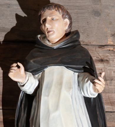 Zdjęcie nr 1: Figura drążona ustawiona na niewielkim, prostopadłościennym postumencie. Święty ukazany całopostaciowo, frontalnie z sylwetką wygiętą w kształt litery „S”, z rękoma lekko zgiętymi w łokciach i uniesionymi do góry. Twarz owalna z wyraźnie zaakcentowanymi kośćmi policzkowymi, karnacja jasna. Oczy szeroko otwarte, wpatrzone przed siebie, usta lekko rozchylone.
Włosy koloru brązowego. Na głowie widoczna tonsura. Święty ubrany jest w biały habit dominikański ze szkaplerzem oraz czarny płaszcz z kapturem. Spod habitu widoczne są brązowe buty. Szaty podkreślające anatomię. Figura w pełni polichromowana.