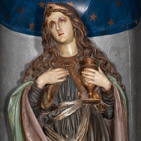 Zdjęcie nr 1: Rzeźba pełnoplastyczna, całopostaciowa, przyścienna, drążona z tyłu. Św. Maria Magdalena ukazana została w pozycji stojącej, z lekko zgiętą w kolanie, wysuniętą do przodu prawą nogą. Prawa ręka zgięta w łokciu spoczywa na piersi, w lewej dłoni święta trzyma kielich. Jej głowa jest lekko zwrócona w prawą stronę, a wzrok skierowany ku górze. Długie pofalowane włosy opadają na ramiona. Na głowie św. Maria Magdalena nałożoną ma złoty diadem. Postać ubrana jest w długą szatę, z długimi rękawami, w kolorze szaroniebieskim, zdobioną złotą lamówką. Biodra świętej przepasane są szarfą w kolorze złotym. Na ramiona narzucony ma błękitny płaszcz, spięty pod szyją klamrą. Poły płaszcza przytrzymywane są przez św. Marie Magdalenę na przedramionach i spływają po zewnętrznych ich stronach. Prawa poła płaszcza zakrywa prawe kolano, wywijając się i ukazując różowe podbicie. U stóp Świętej, po lewej stronie znajduje się czaszka.