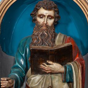 Zdjęcie nr 1: Rzeźba pełnoplastyczna, przyścienna. Święty Paweł ukazany został w całej postaci, frontalnie, w pozycji stojącej, z lewą nogą wspartą na skale. W lewej dłoni trzyma otwartą księgę, zaś w prawej niegdyś znajdował się miecz. Głowa świętego jest lekko pochylona w lewą stronę, a wzrok opuszczony na karty księgi. Ubrany jest w niebieską szatę z długimi rękawami, spływającą do stóp. Szata dekorowana jest złotą lamówką. Na ramiona św. Paweł narzucony ma czerwony płaszcz, z jasnym podbiciem. Wierzchnie odzienie dekorowane jest złotą lamówką i złotym ornamentem roślinnym w formie pasa biegnącego wzdłuż jego krawędzi. Poła płaszcza przerzucona jest przez lewe ramię świętego, spływa z lewego przedramienia i podtrzymywana jest na wysokości brzucha, gdzie odwija się ukazując podszewkę. Postać ma wyraziste rysy twarzy, długi, wąski nos, lekko pofalowane, brązowe włosy przykrywające uszy, oraz brązowe wąsy i długą brodę.