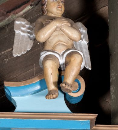 Zdjęcie nr 4: Nastawa ołtarzowa architektoniczna, jednoosiowa, jednokondygnacyjna, ze zwieńczeniem. Ołtarz drewniany, sarkofagowy, zwężający się ku dołowi, na cokole. Mensa drewniana, silnie wysunięta.  Antependium w kształcie trapezu, w polu romb ujęty obramieniem, z rozetą, flankowany dwoma rombami. Retabulum na dwustrefowym cokole, flankowane para półfilarów o stylizowanych kapitelach kompozytowych i kanelowanych trzonach, umieszczonych na cokołach nadwieszonych na konsolach. Podpory dźwigają pełne belkowanie, występujące na ich osi, z silnie wysuniętym, bogato profilowanym gzymsem, nad polem środkowym wyłamanym trójbocznie. W zwieńczeniu w osiach podpór odcinki przerwanego przyczółka, na których siedzą dwa uskrzydlone putta. W polu środkowym nisza w kształcie stojącego prostokąta zamkniętego łukiem nadwieszonym z uskokiem, ujęta profilowaną ramą; wewnątrz profilowana rama w kształcie stojącego prostokąta, w której znajduje się obraz Matki Boskiej z Dzieciątkiem w ramie dekorowanej płaskorzeźbionymi motywami liści akantu. W zwieńczeniu, nad polem środkowym medalion z ze splecionymi literami imienia Marya w glorii promienistej, u dołu motyw rocaille’u. W górnej strefie cokołu dwie płyciny w formie leżącego prostokąta z rozetami; cokoły kolumn zdobione z trzech stron płycinami z malowaną dekoracją roślinną. W partii fryzu na osi podpór rozety. Rama niszy zwieńczona motywem rocaille’u. Retabulum ujęte uszami utworzonymi z motywów stylizowanych liści akantu i elementów małżowiny. Struktura polichromowana w kolorze jasnoniebieskim, profile na niebiesko; konsole i trzony marmoryzowane; ornamentyka, ramy, profile i gloria złocone.