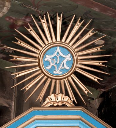 Zdjęcie nr 6: Nastawa ołtarzowa architektoniczna, jednoosiowa, jednokondygnacyjna, ze zwieńczeniem. Ołtarz drewniany, sarkofagowy, zwężający się ku dołowi, na cokole. Mensa drewniana, silnie wysunięta.  Antependium w kształcie trapezu, w polu romb ujęty obramieniem, z rozetą, flankowany dwoma rombami. Retabulum na dwustrefowym cokole, flankowane para półfilarów o stylizowanych kapitelach kompozytowych i kanelowanych trzonach, umieszczonych na cokołach nadwieszonych na konsolach. Podpory dźwigają pełne belkowanie, występujące na ich osi, z silnie wysuniętym, bogato profilowanym gzymsem, nad polem środkowym wyłamanym trójbocznie. W zwieńczeniu w osiach podpór odcinki przerwanego przyczółka, na których siedzą dwa uskrzydlone putta. W polu środkowym nisza w kształcie stojącego prostokąta zamkniętego łukiem nadwieszonym z uskokiem, ujęta profilowaną ramą; wewnątrz profilowana rama w kształcie stojącego prostokąta, w której znajduje się obraz Matki Boskiej z Dzieciątkiem w ramie dekorowanej płaskorzeźbionymi motywami liści akantu. W zwieńczeniu, nad polem środkowym medalion z ze splecionymi literami imienia Marya w glorii promienistej, u dołu motyw rocaille’u. W górnej strefie cokołu dwie płyciny w formie leżącego prostokąta z rozetami; cokoły kolumn zdobione z trzech stron płycinami z malowaną dekoracją roślinną. W partii fryzu na osi podpór rozety. Rama niszy zwieńczona motywem rocaille’u. Retabulum ujęte uszami utworzonymi z motywów stylizowanych liści akantu i elementów małżowiny. Struktura polichromowana w kolorze jasnoniebieskim, profile na niebiesko; konsole i trzony marmoryzowane; ornamentyka, ramy, profile i gloria złocone.