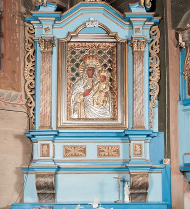Zdjęcie nr 1: Nastawa ołtarzowa architektoniczna, jednoosiowa, jednokondygnacyjna, ze zwieńczeniem. Ołtarz drewniany, sarkofagowy, zwężający się ku dołowi, na cokole. Mensa drewniana, silnie wysunięta.  Antependium w kształcie trapezu, w polu romb ujęty obramieniem, z rozetą, flankowany dwoma rombami. Retabulum na dwustrefowym cokole, flankowane para półfilarów o stylizowanych kapitelach kompozytowych i kanelowanych trzonach, umieszczonych na cokołach nadwieszonych na konsolach. Podpory dźwigają pełne belkowanie, występujące na ich osi, z silnie wysuniętym, bogato profilowanym gzymsem, nad polem środkowym wyłamanym trójbocznie. W zwieńczeniu w osiach podpór odcinki przerwanego przyczółka, na których siedzą dwa uskrzydlone putta. W polu środkowym nisza w kształcie stojącego prostokąta zamkniętego łukiem nadwieszonym z uskokiem, ujęta profilowaną ramą; wewnątrz profilowana rama w kształcie stojącego prostokąta, w której znajduje się obraz Matki Boskiej z Dzieciątkiem w ramie dekorowanej płaskorzeźbionymi motywami liści akantu. W zwieńczeniu, nad polem środkowym medalion z ze splecionymi literami imienia Marya w glorii promienistej, u dołu motyw rocaille’u. W górnej strefie cokołu dwie płyciny w formie leżącego prostokąta z rozetami; cokoły kolumn zdobione z trzech stron płycinami z malowaną dekoracją roślinną. W partii fryzu na osi podpór rozety. Rama niszy zwieńczona motywem rocaille’u. Retabulum ujęte uszami utworzonymi z motywów stylizowanych liści akantu i elementów małżowiny. Struktura polichromowana w kolorze jasnoniebieskim, profile na niebiesko; konsole i trzony marmoryzowane; ornamentyka, ramy, profile i gloria złocone.