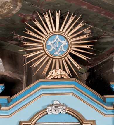 Zdjęcie nr 5: Nastawa ołtarzowa architektoniczna, jednoosiowa, jednokondygnacyjna, ze zwieńczeniem. Ołtarz drewniany, sarkofagowy, zwężający się ku dołowi, na cokole. Mensa drewniana, silnie wysunięta.  Antependium w kształcie trapezu, w polu romb ujęty obramieniem, z rozetą, flankowany dwoma rombami. Retabulum na dwustrefowym cokole, flankowane para półfilarów o stylizowanych kapitelach kompozytowych i kanelowanych trzonach, umieszczonych na cokołach nadwieszonych na konsolach. Podpory dźwigają pełne belkowanie, występujące na ich osi, z silnie wysuniętym, bogato profilowanym gzymsem, nad polem środkowym wyłamanym trójbocznie. W zwieńczeniu w osiach podpór odcinki przerwanego przyczółka, na których siedzą dwa uskrzydlone putta. W polu środkowym nisza w kształcie stojącego prostokąta zamkniętego łukiem nadwieszonym z uskokiem, ujęta profilowaną ramą; wewnątrz profilowana rama w kształcie stojącego prostokąta, w której znajduje się obraz Matki Boskiej z Dzieciątkiem w ramie dekorowanej płaskorzeźbionymi motywami liści akantu. W zwieńczeniu, nad polem środkowym medalion z ze splecionymi literami imienia Marya w glorii promienistej, u dołu motyw rocaille’u. W górnej strefie cokołu dwie płyciny w formie leżącego prostokąta z rozetami; cokoły kolumn zdobione z trzech stron płycinami z malowaną dekoracją roślinną. W partii fryzu na osi podpór rozety. Rama niszy zwieńczona motywem rocaille’u. Retabulum ujęte uszami utworzonymi z motywów stylizowanych liści akantu i elementów małżowiny. Struktura polichromowana w kolorze jasnoniebieskim, profile na niebiesko; konsole i trzony marmoryzowane; ornamentyka, ramy, profile i gloria złocone.