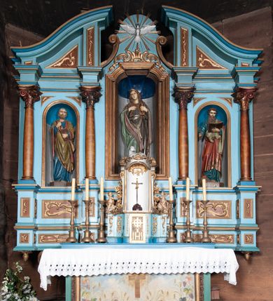 Zdjęcie nr 4: Retabulum ołtarzowe trójosiowe, na dwustrefowym cokole, jednokondygnacyjne, ze zwieńczeniem. Nastawa szersza od ołtarza, artykułowana jest kolumnami o gładkich trzonach i kompozytowych kapitelach, podtrzymującymi występujące się nad nią uproszczone belkowanie i gzyms. W polach pomiędzy kolumnami prostokątne nisze, pośrodku zamknięta uskokowo, w niej rzeźba patronki świątyni św. Marii Magdaleny; nisze w polach bocznych zamknięte półkoliście, w nich rzeźby św. Piotra i św. Pawła. W zwieńczeniu przerwany przyczółek zamknięty łukiem wklęsło-wypukłym, w osiach wewnętrznych kolumn wsparty na lizenach. W osi środkowej rzeźbiona Gołębica Ducha Świętego w glorii promienistej ujętej po bokach wolutami i od dołu motywami ornamentu małżowinowego. W części cokołowej w płycinach ujętych ramami umieszczono motywy ornamentu rocaille’owego. W przyczółku w płycinach motywy liści akantu. 
Na mensie tabernakulum połączone z Tronem Łaski do wystawienia monstrancji, na rzucie prostokąta, dwustrefowe, z dolną strefą ujętą wklęsłymi ściankami parawanowymi. W dolnej części tabernakulum znajdują się prostokątne drzwiczki z krzyżem i literami: IHS. Drzwiczki są ujęte kampanulami oraz ornamentem rocaille’owym. Tron wystawienia ujęto spływami wolutowymi w formie krzewu różanego, zakończonymi adorującymi uskrzydlonymi aniołami umieszczonymi na obłokach. Część środkowa tronu wystawienia jest obrotowa. Górną jego część zakończono łukiem wklęsło-wypukłym, i ozdobiono ornamentem kartuszowo-zawijanym oraz figurą leżącego baranka. Antependium prostokątne, malowane na płótnie, ujęte w drewniane ramy zdobione wicią roślinną. W centralnej części ukazany został krzyż na tle promieni, po bokach winna latorośl i kłosy zboża. 