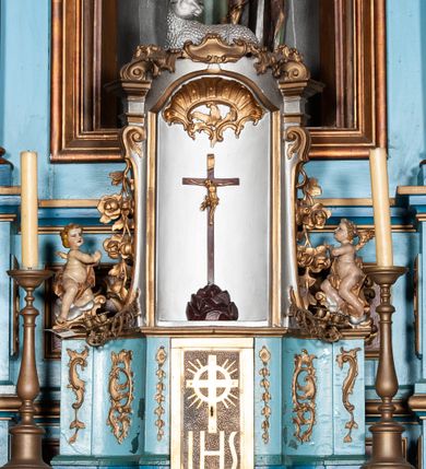 Zdjęcie nr 5: Retabulum ołtarzowe trójosiowe, na dwustrefowym cokole, jednokondygnacyjne, ze zwieńczeniem. Nastawa szersza od ołtarza, artykułowana jest kolumnami o gładkich trzonach i kompozytowych kapitelach, podtrzymującymi występujące się nad nią uproszczone belkowanie i gzyms. W polach pomiędzy kolumnami prostokątne nisze, pośrodku zamknięta uskokowo, w niej rzeźba patronki świątyni św. Marii Magdaleny; nisze w polach bocznych zamknięte półkoliście, w nich rzeźby św. Piotra i św. Pawła. W zwieńczeniu przerwany przyczółek zamknięty łukiem wklęsło-wypukłym, w osiach wewnętrznych kolumn wsparty na lizenach. W osi środkowej rzeźbiona Gołębica Ducha Świętego w glorii promienistej ujętej po bokach wolutami i od dołu motywami ornamentu małżowinowego. W części cokołowej w płycinach ujętych ramami umieszczono motywy ornamentu rocaille’owego. W przyczółku w płycinach motywy liści akantu. 
Na mensie tabernakulum połączone z Tronem Łaski do wystawienia monstrancji, na rzucie prostokąta, dwustrefowe, z dolną strefą ujętą wklęsłymi ściankami parawanowymi. W dolnej części tabernakulum znajdują się prostokątne drzwiczki z krzyżem i literami: IHS. Drzwiczki są ujęte kampanulami oraz ornamentem rocaille’owym. Tron wystawienia ujęto spływami wolutowymi w formie krzewu różanego, zakończonymi adorującymi uskrzydlonymi aniołami umieszczonymi na obłokach. Część środkowa tronu wystawienia jest obrotowa. Górną jego część zakończono łukiem wklęsło-wypukłym, i ozdobiono ornamentem kartuszowo-zawijanym oraz figurą leżącego baranka. Antependium prostokątne, malowane na płótnie, ujęte w drewniane ramy zdobione wicią roślinną. W centralnej części ukazany został krzyż na tle promieni, po bokach winna latorośl i kłosy zboża. 