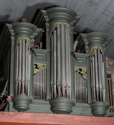 Zdjęcie nr 1: Prospekt organowy architektoniczny, pięcioosiowy, z wydzielonym cokołem. W osi środkowej i skrajnych ryzality półcylindryczne (środkowy wyższy i szerszy) z prześwitami, nadwieszone na profilowanych konsolach  i zwieńczone uproszczonym belkowaniem i profilowanymi gzymsami. W osiach wewnętrznych prostokątne prześwity zwieńczone prostokątnymi płycinami i odcinkami profilowanego gzymsu. Prześwity wypełnione piszczałkami; zwieńczone niepełnym belkowaniem, z profilowanym, silnie wysuniętym gzymsem. Wszystkie prześwity w górnej części wypełnione motywami liści akantu. Struktura polichromowana w kolorze niebieskozielonym, ornamenty na biało.