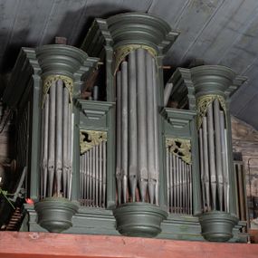 Zdjęcie nr 1: Prospekt organowy architektoniczny, pięcioosiowy, z wydzielonym cokołem. W osi środkowej i skrajnych ryzality półcylindryczne (środkowy wyższy i szerszy) z prześwitami, nadwieszone na profilowanych konsolach  i zwieńczone uproszczonym belkowaniem i profilowanymi gzymsami. W osiach wewnętrznych prostokątne prześwity zwieńczone prostokątnymi płycinami i odcinkami profilowanego gzymsu. Prześwity wypełnione piszczałkami; zwieńczone niepełnym belkowaniem, z profilowanym, silnie wysuniętym gzymsem. Wszystkie prześwity w górnej części wypełnione motywami liści akantu. Struktura polichromowana w kolorze niebieskozielonym, ornamenty na biało.