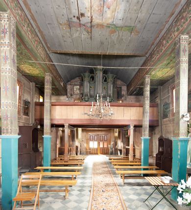 Zdjęcie nr 2: Prospekt organowy architektoniczny, pięcioosiowy, z wydzielonym cokołem. W osi środkowej i skrajnych ryzality półcylindryczne (środkowy wyższy i szerszy) z prześwitami, nadwieszone na profilowanych konsolach  i zwieńczone uproszczonym belkowaniem i profilowanymi gzymsami. W osiach wewnętrznych prostokątne prześwity zwieńczone prostokątnymi płycinami i odcinkami profilowanego gzymsu. Prześwity wypełnione piszczałkami; zwieńczone niepełnym belkowaniem, z profilowanym, silnie wysuniętym gzymsem. Wszystkie prześwity w górnej części wypełnione motywami liści akantu. Struktura polichromowana w kolorze niebieskozielonym, ornamenty na biało.