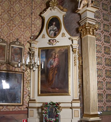 Zdjęcie nr 1: Ołtarz architektoniczny, jednoosiowy, jednokondygnacyjny ze zwieńczeniem, z uszami. Retabulum ustawione na prostopadłościennej mensie ołtarzowej z antepedium, zdobionym czterema prostokątnymi płycinami oddzielonymi kanelowanymi lizenami. Tabernakulum w kształcie prostopadłościennej skrzynki na wysokim cokole, zamkniętej od góry płaskim daszkiem, na którym miejsce na prosty tron do wystawiania monstrancji. Przednia ścianka tabernakulum zamknięta od góry gzymsem w formie łuku nadwieszonego. Drzwiczki w formie stojącego prostokąta zamkniętego łukiem półkolistym. W polu, obwiedzionym ramą o analogicznym kształcie płaskorzeźbiony krzyż z podstawą. Ustawiona na mensie nastawa wsparta na cokole z wyodrębnionymi po bokach dwoma postumentami, wyżej ujęta parą pilastrów, o trzonach ozdobionych płycinami i u góry zwisami ze stylizowanych kampanul, z nałożonymi u szczytu konsolkami pełniącymi funkcję kapiteli, które wspierają odcinki przerwanego belkowania. W polu głównym obraz św. Józefa z Dzieciątkiem Jezus w kształcie pionowego prostokąta. Zwieńczenie  w ogólnym zarysie w kształcie trapezu, o bokach zaakcentowanych wklęsłymi łukami odcinkowymi, zamknięte od góry dwiema wolutkami, spiętymi u szczytu muszlą palmetową i ozdobionymi wicią z różami. W polu owalny obraz z przedstawieniem św. Wiktorii. Poniżej dwie uskrzydlone główki aniołków. Uszy z wici i motywów ornamentu rocaille&#039;owego. Struktura ołtarza w kolorze białym, detale i ornamentyka złocone.